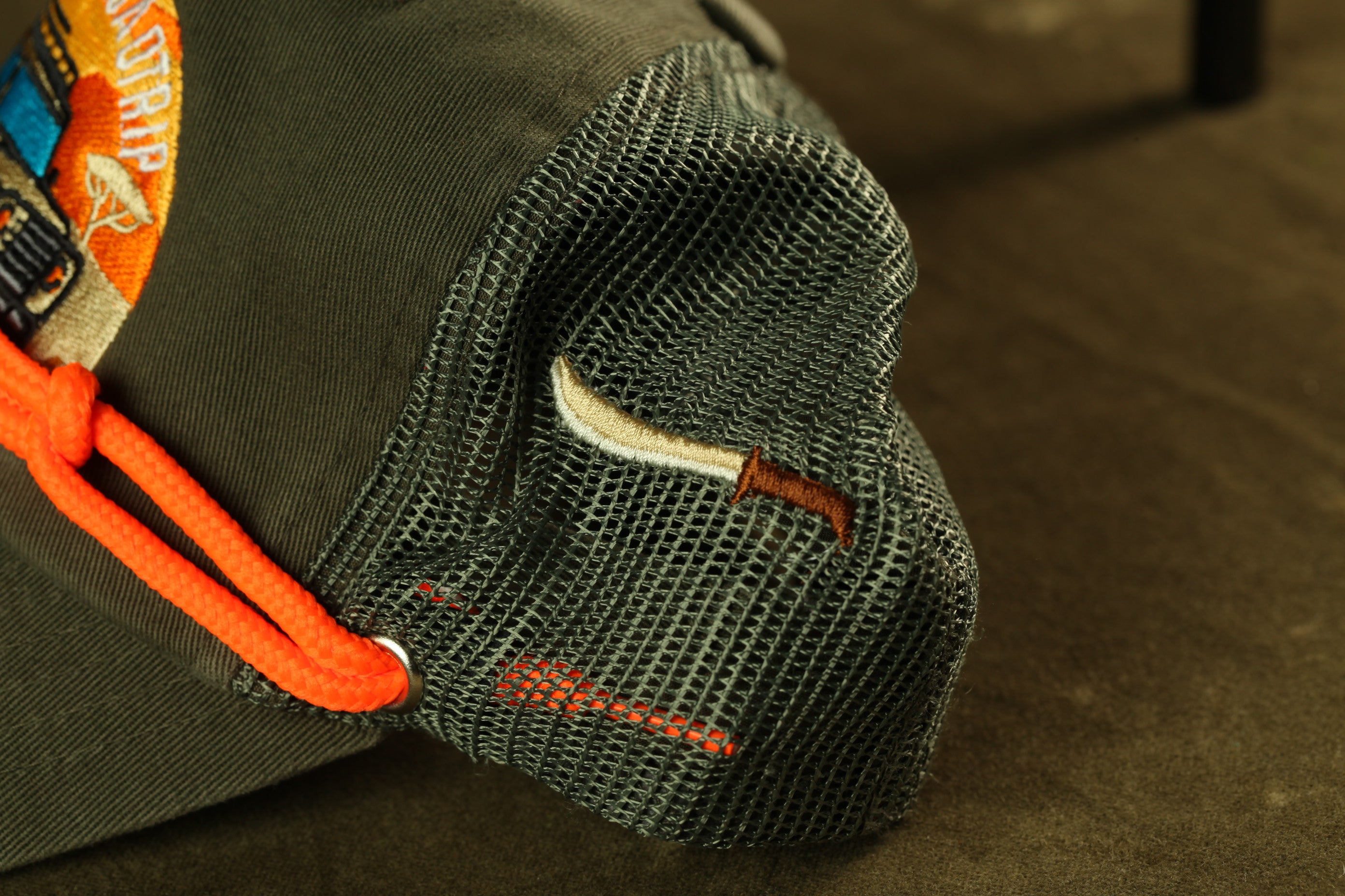 A close-up view of a green mesh hat with an orange string, showing the mesh material and the string.