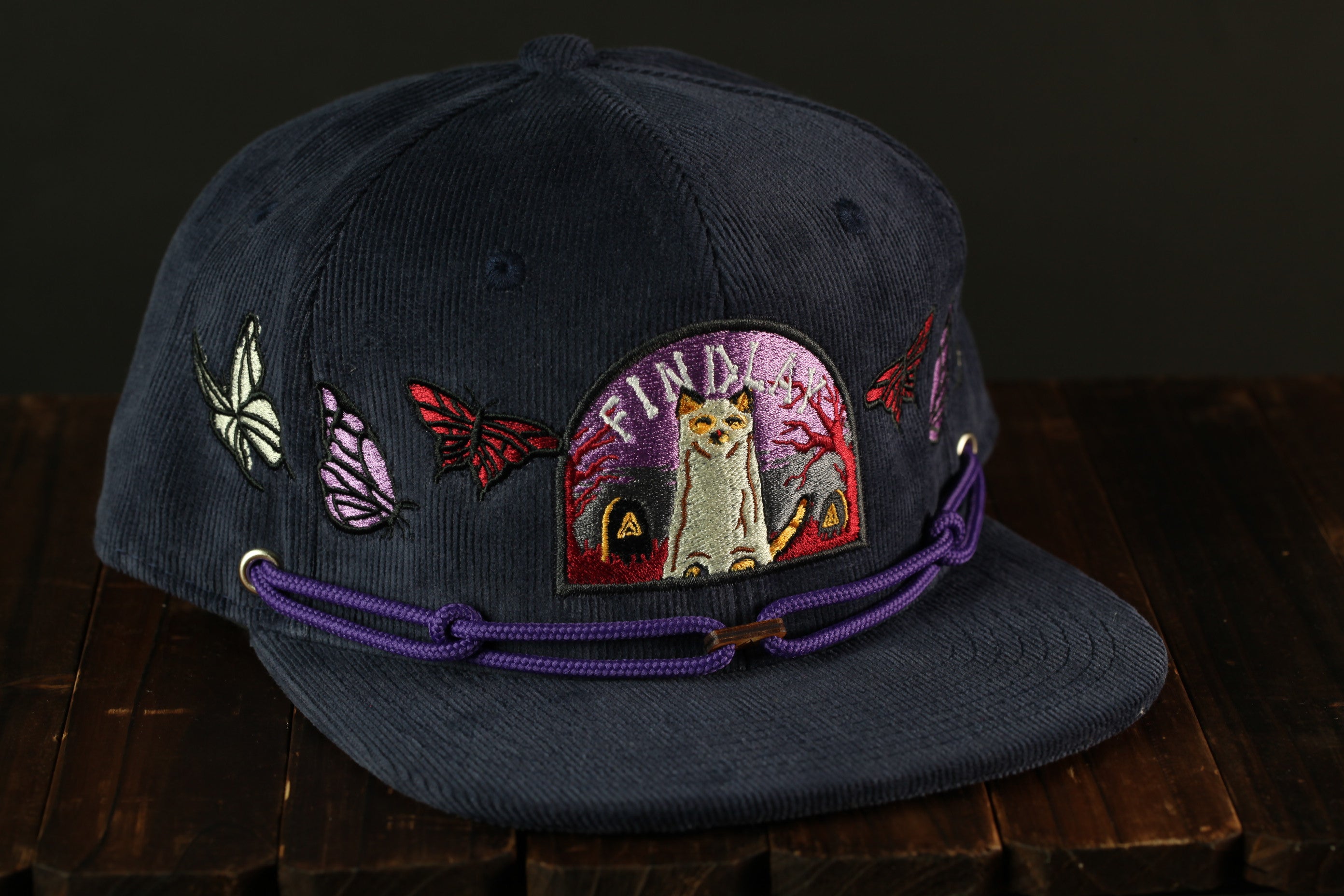 A navy blue baseball cap with a purple band and various colorful butterfly and cat embroidered designs.