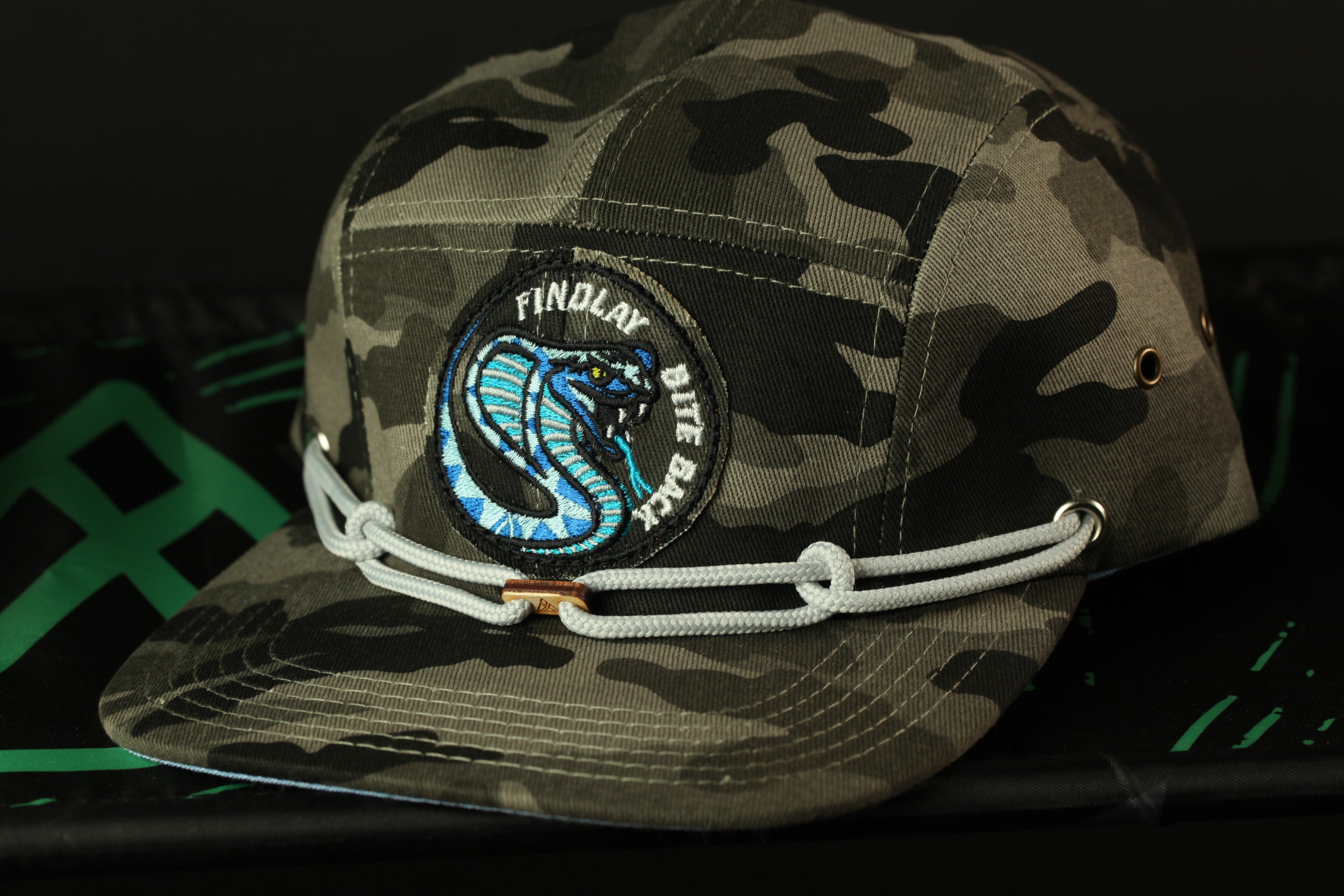 A camouflage baseball cap with a snake design and a patch on the front.