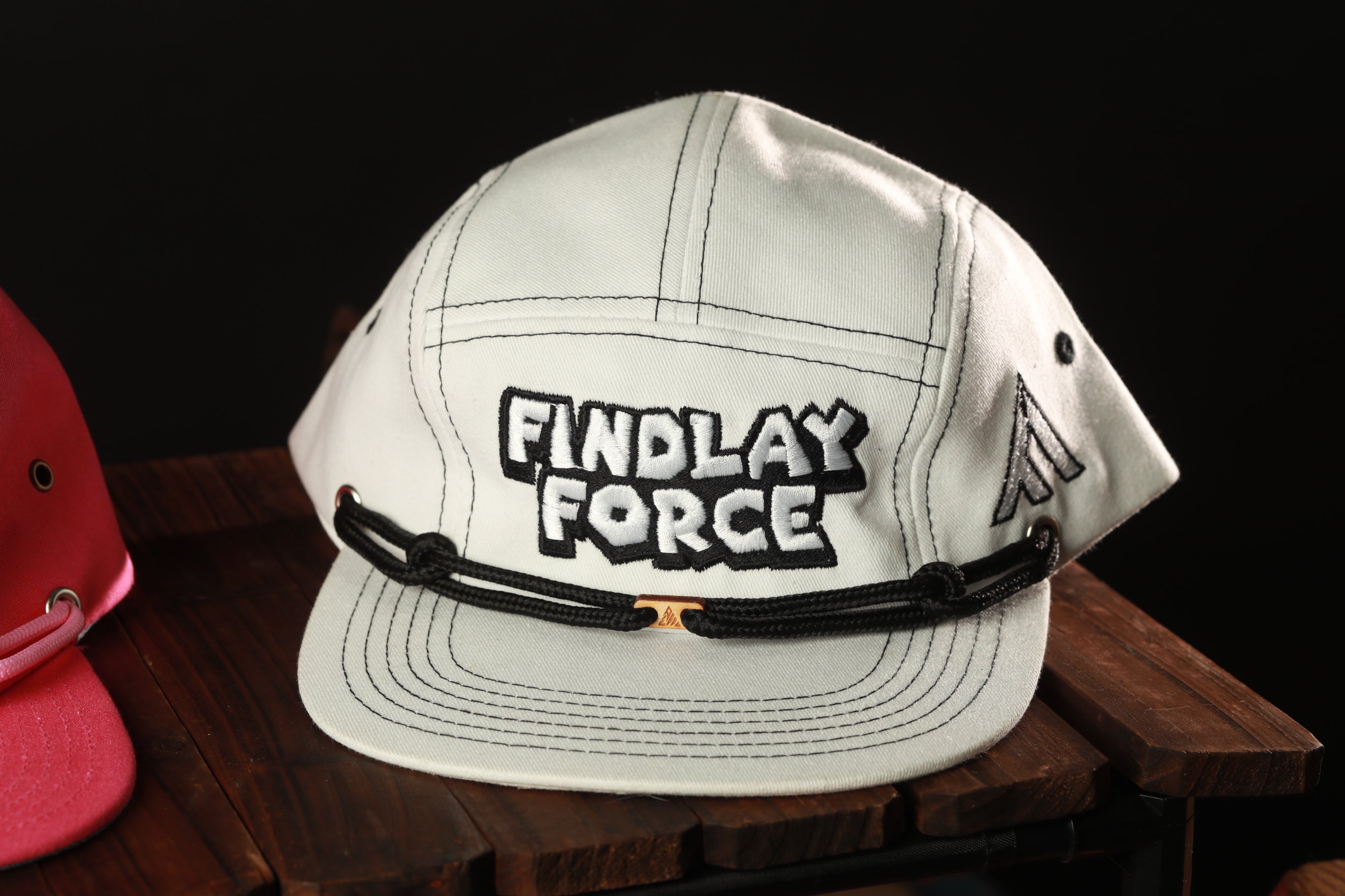 A white baseball cap with the text "FINDLAY FORCE" printed on it, sitting on a wooden surface.