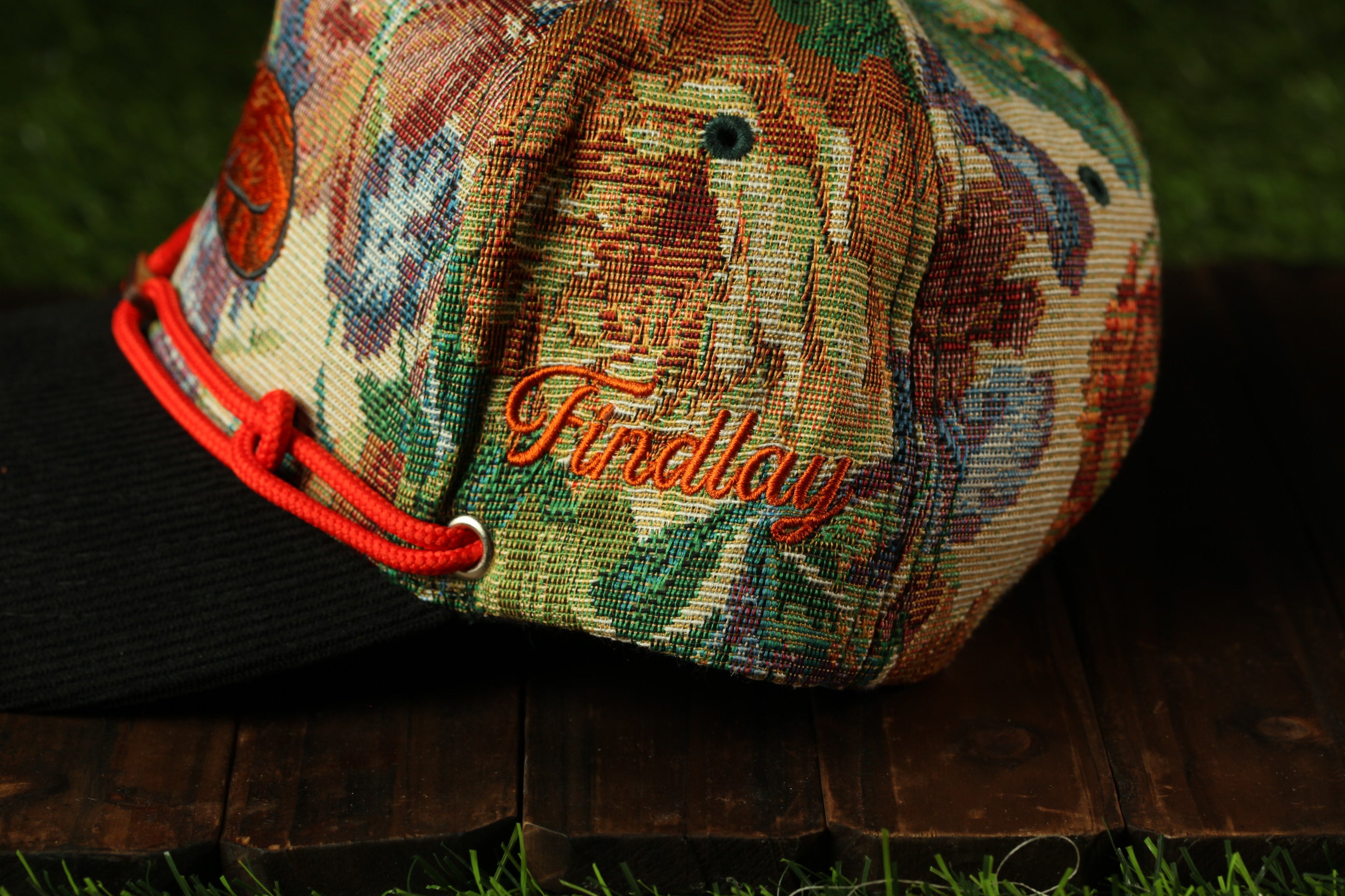 A colorful, patterned baseball cap with the name "Firday" embroidered on it, resting on a wooden surface.