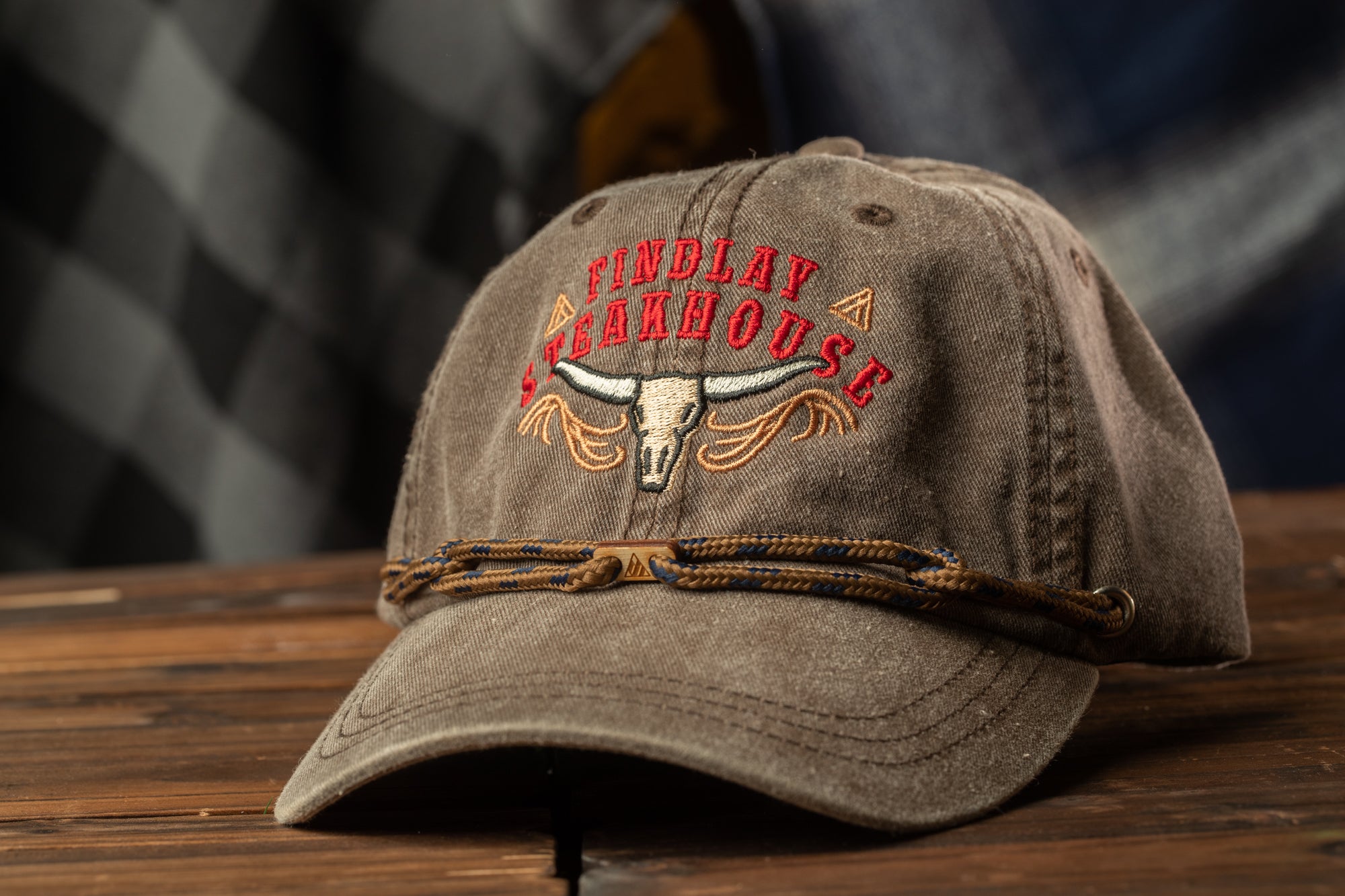 A brown baseball cap with a logo on it, sitting on a wooden surface.