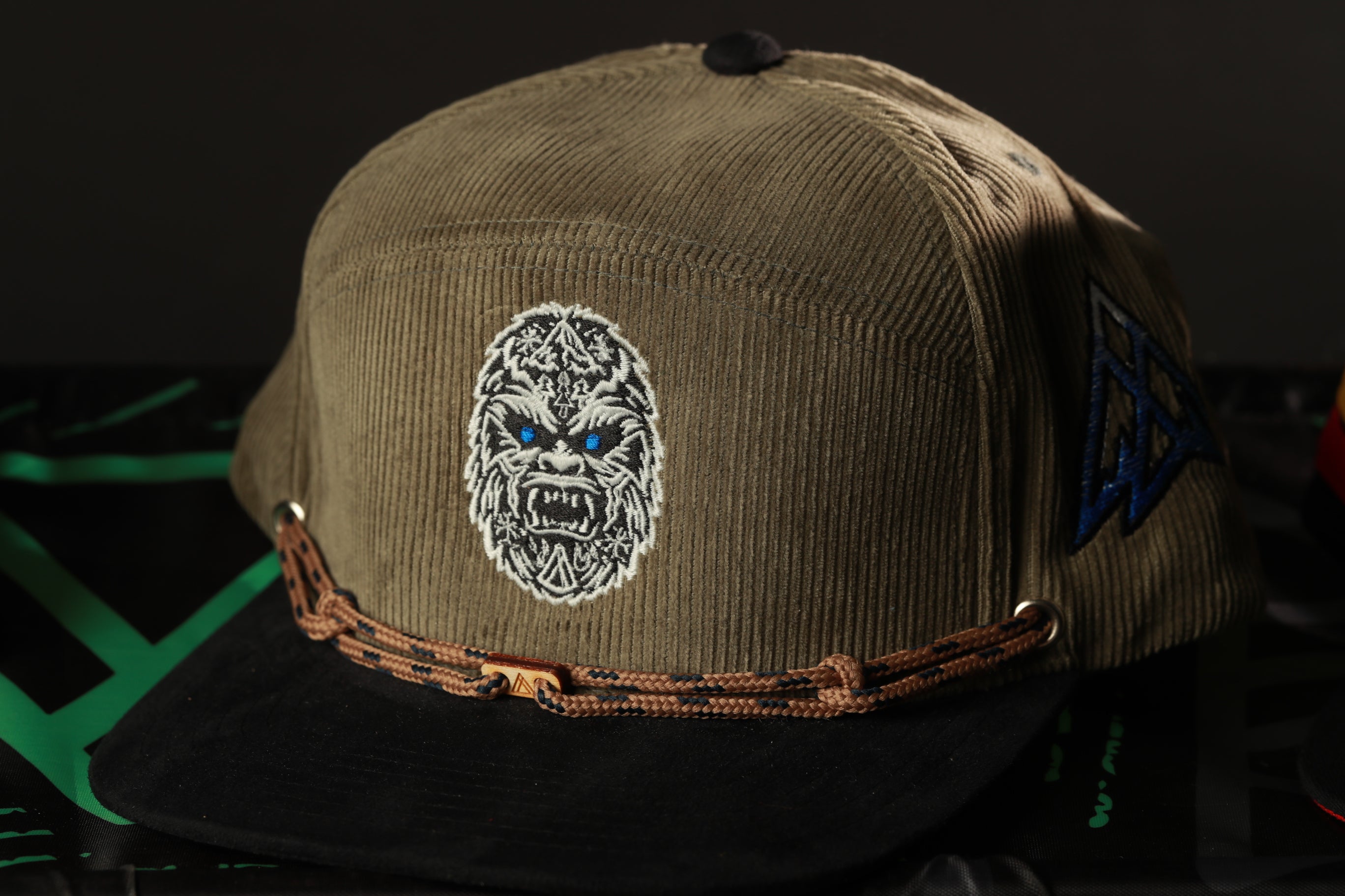 A brown baseball cap with a white gorilla face embroidered on it, along with a brown braided strap.