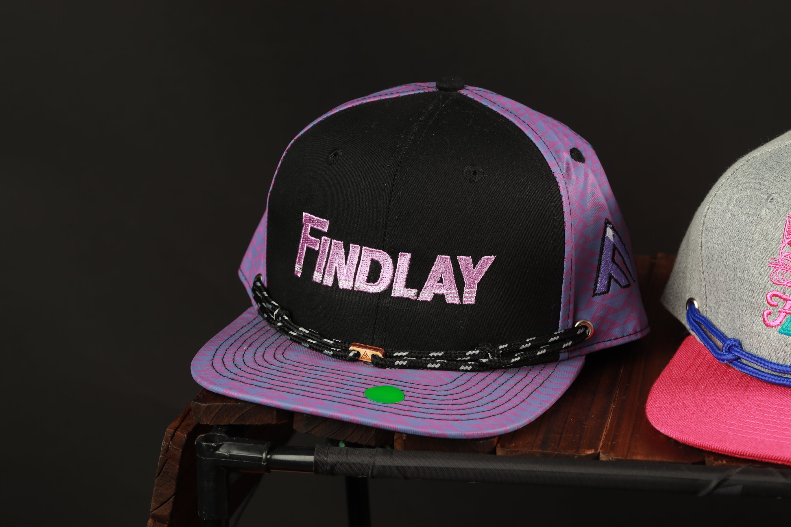 A black and purple baseball cap with the word "FINDlay" printed on it, sitting on a wooden surface.