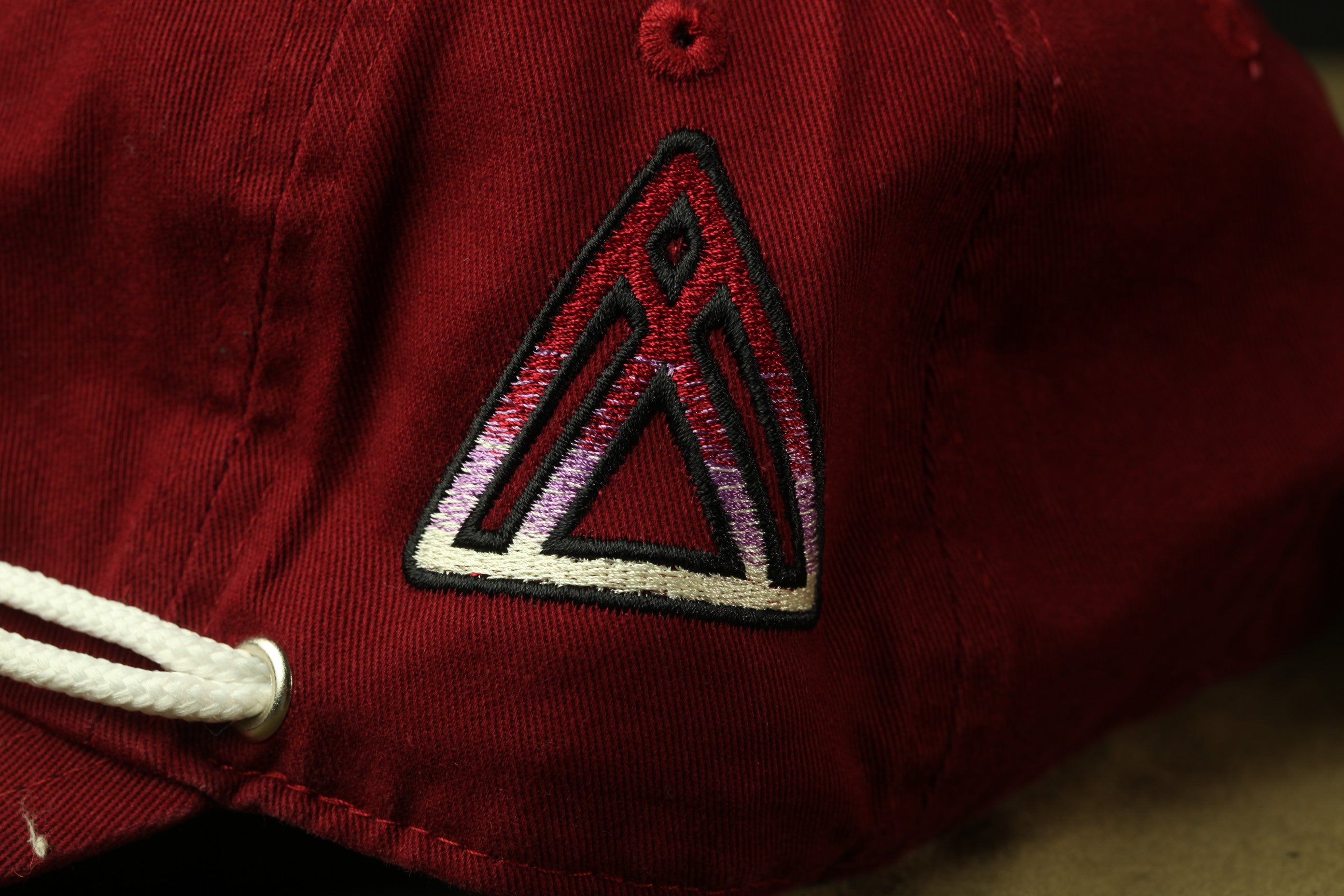 A close-up view of a red baseball cap with a white triangle-shaped logo on the front.