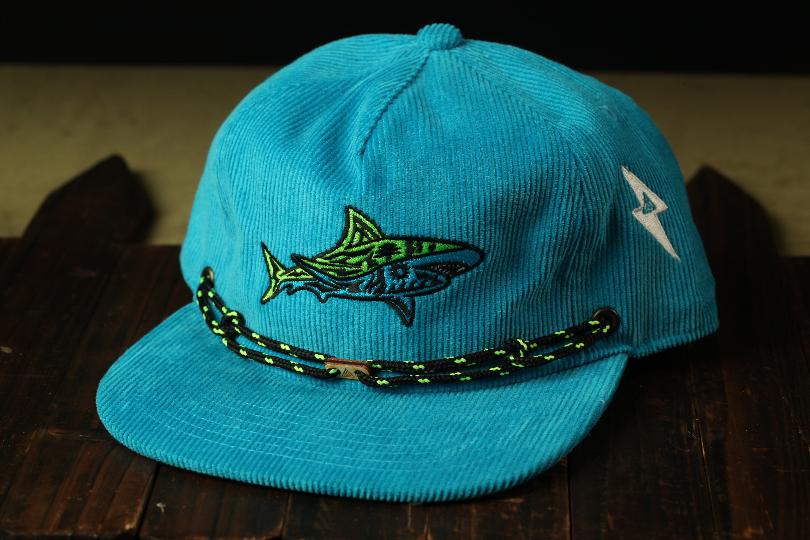 A blue baseball cap with a shark embroidered on it, sitting on a wooden surface.