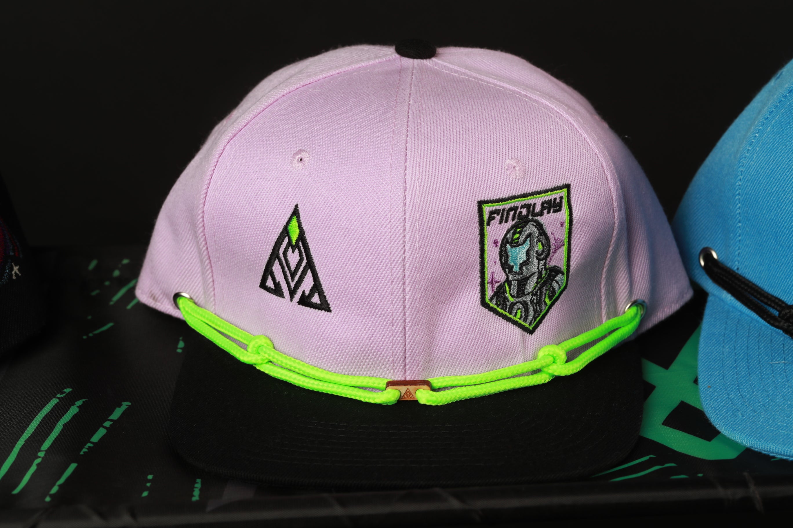 A pink baseball cap with a graphic design and a patch featuring a character, placed on a black surface.