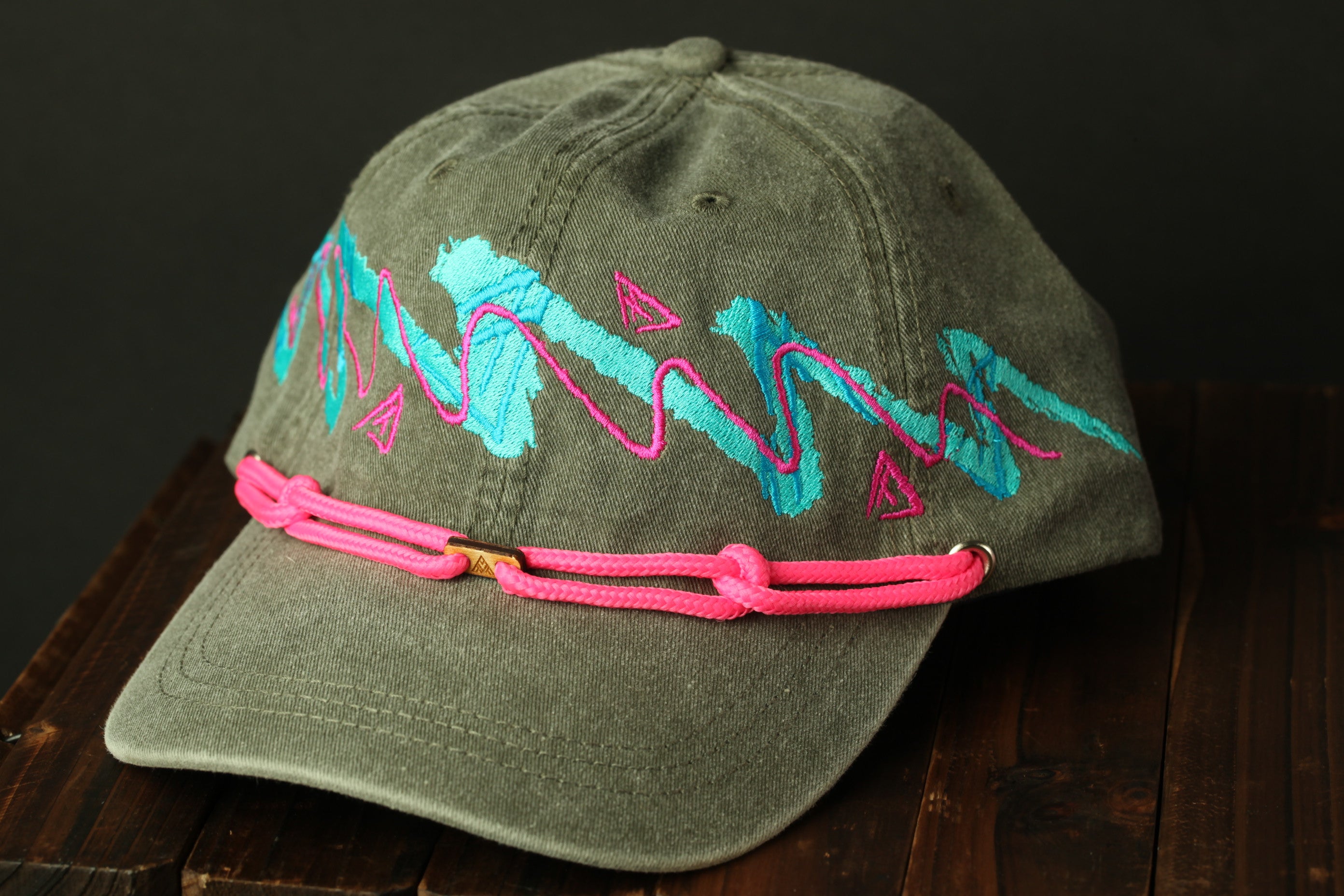 A gray baseball cap with a pink braided strap and colorful embroidered designs on the front.