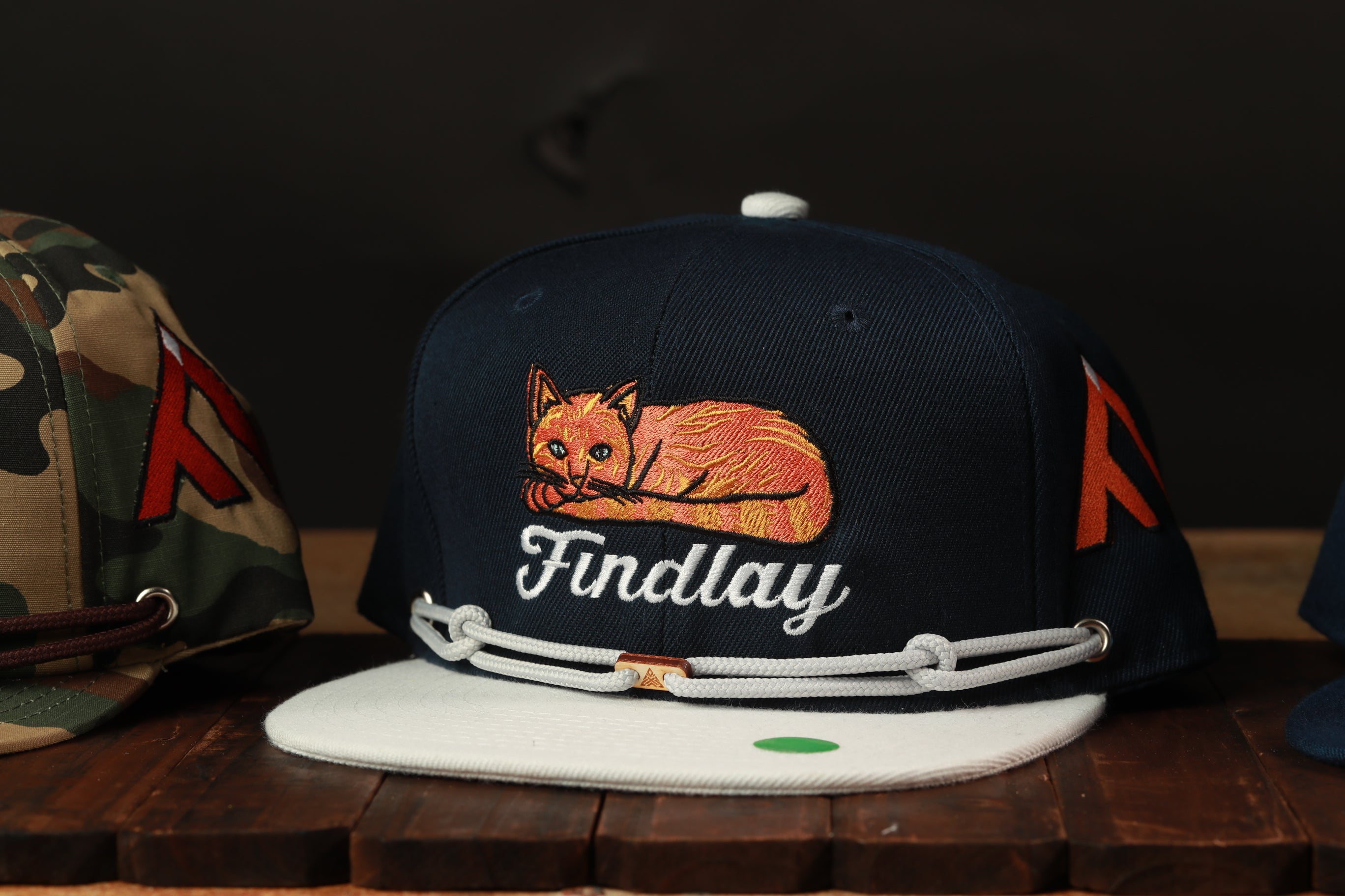 A navy blue baseball cap with a cat embroidered on it, featuring the name 'Findlay' on the front.