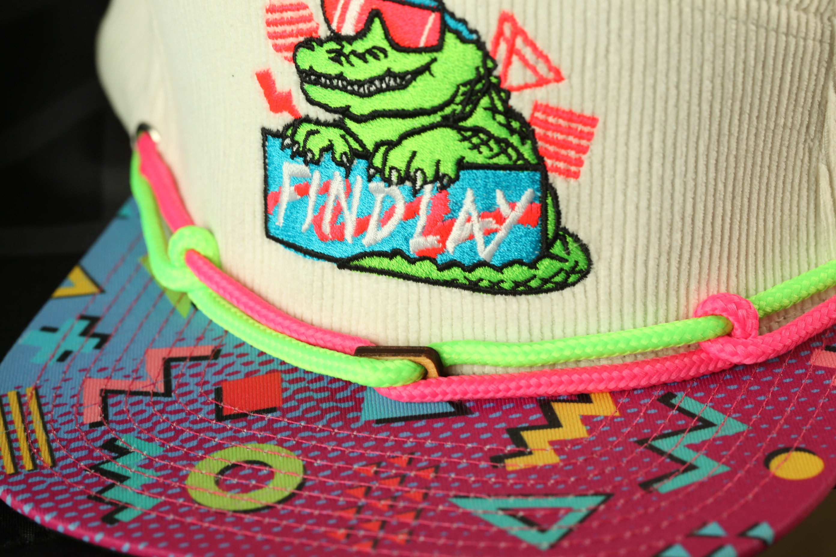 A close-up of a colorful baseball cap with a cartoon character and neon-colored strings.