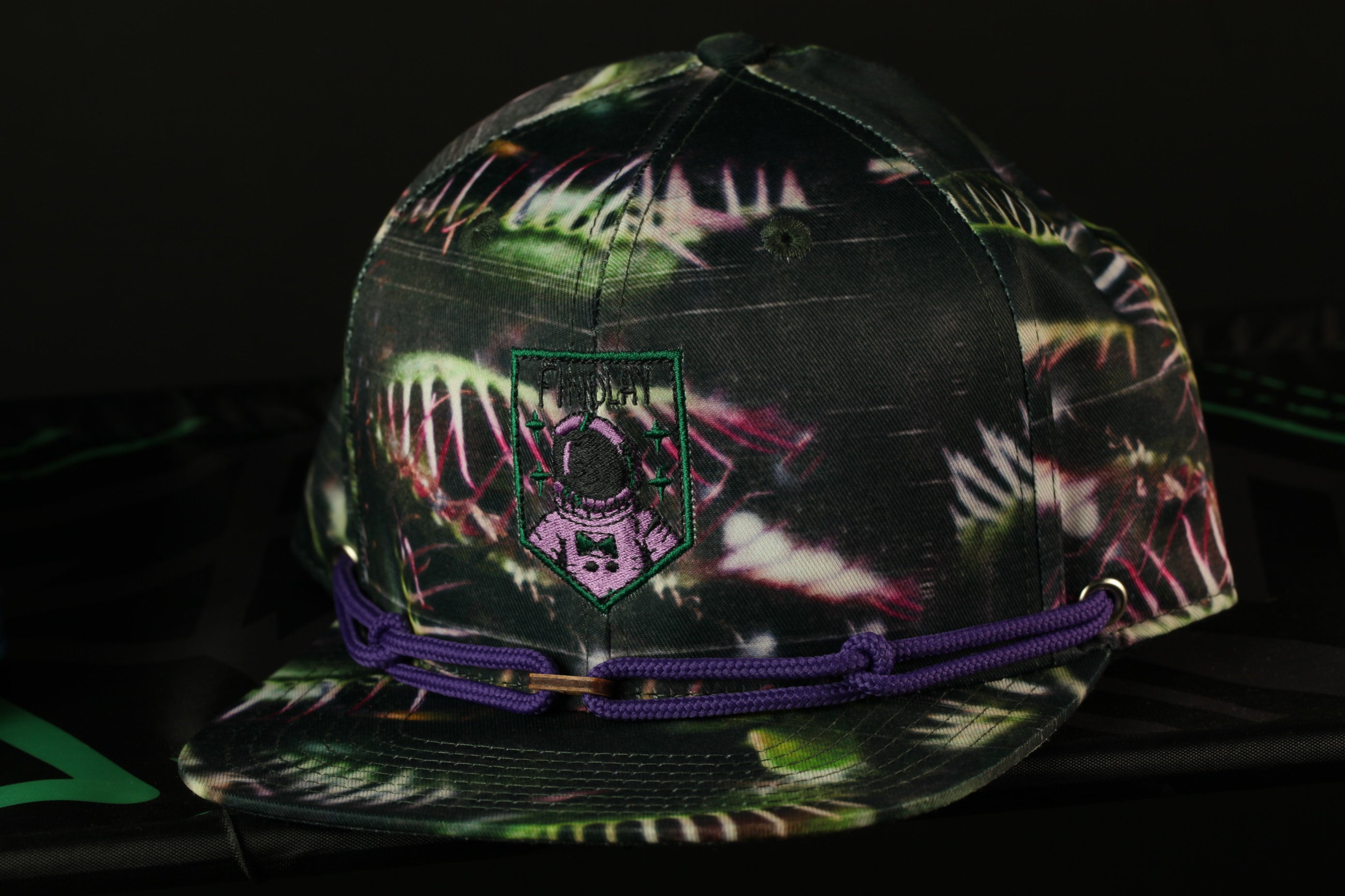 A camouflage baseball cap with a purple band and a green and purple patterned design.