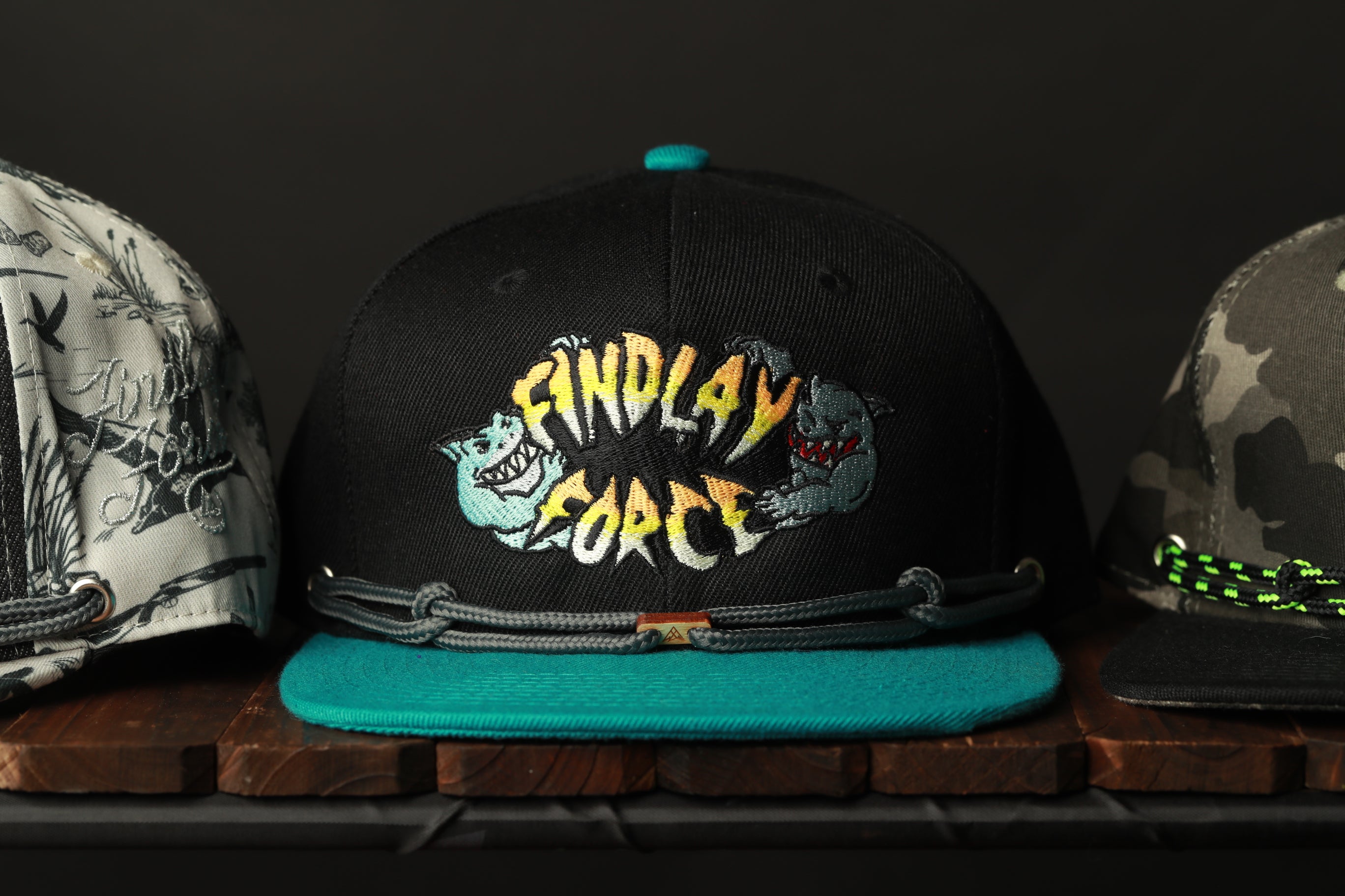 A collection of three baseball caps, each with a unique design, displayed on a wooden surface.