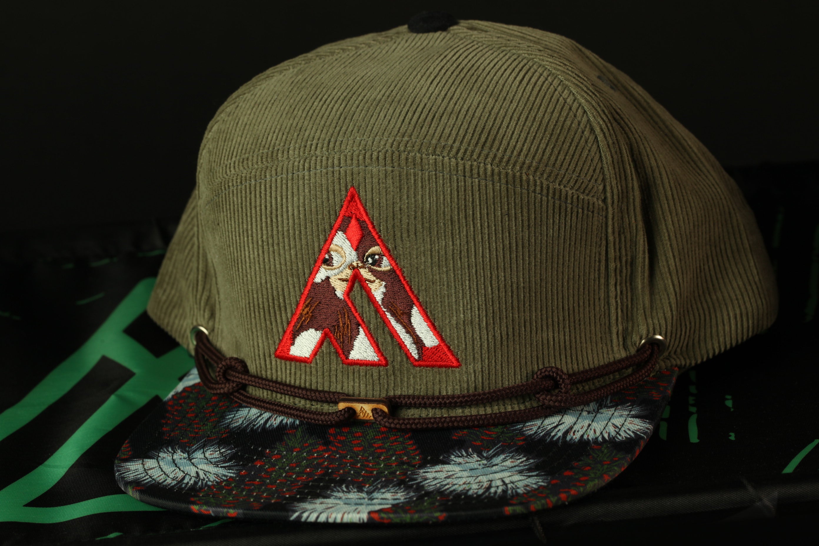 A green baseball cap with a red and white embroidered logo on the front, placed on a black surface.