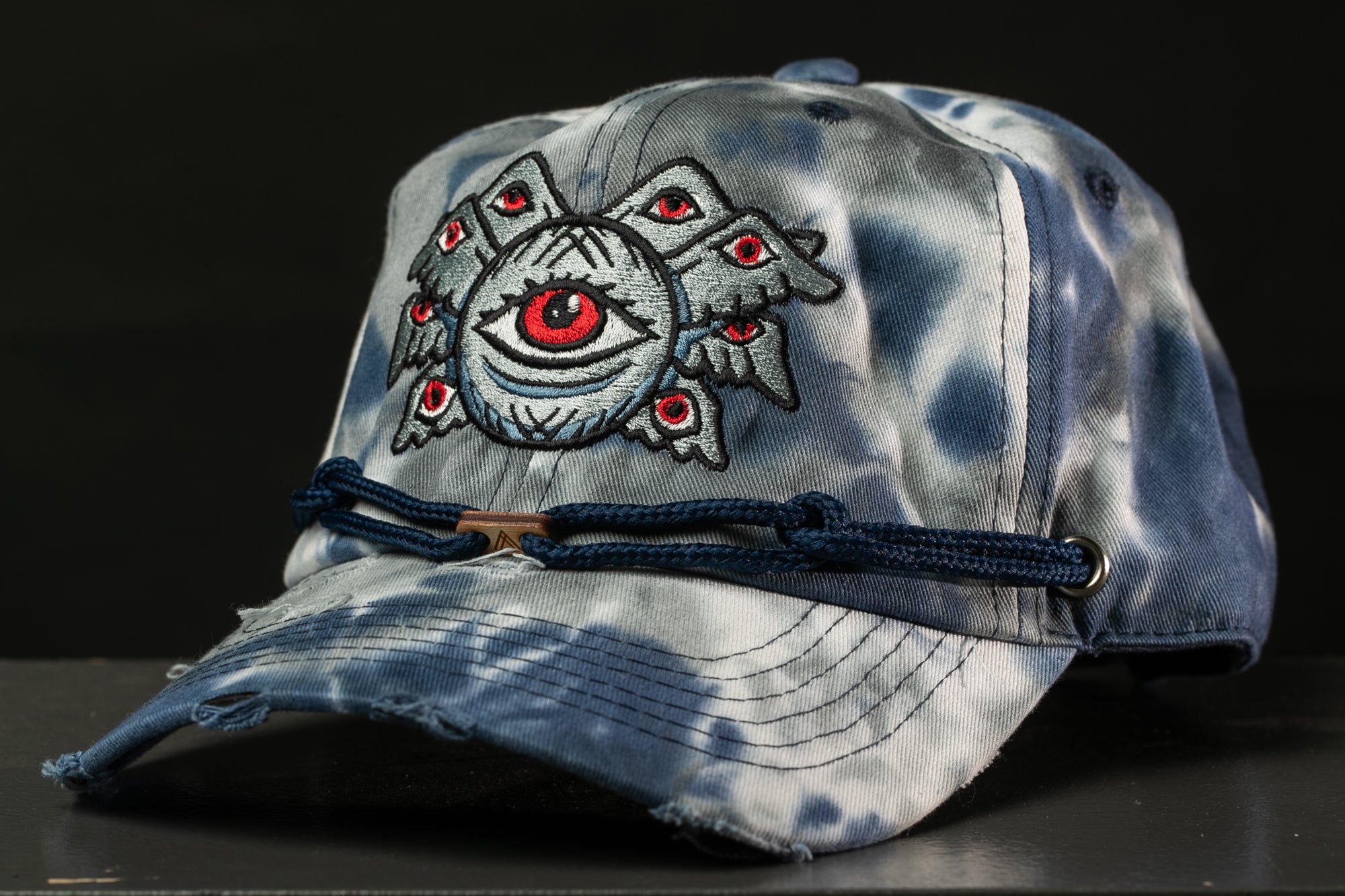 A blue and gray tie-dye baseball cap with an eye design on the front.
