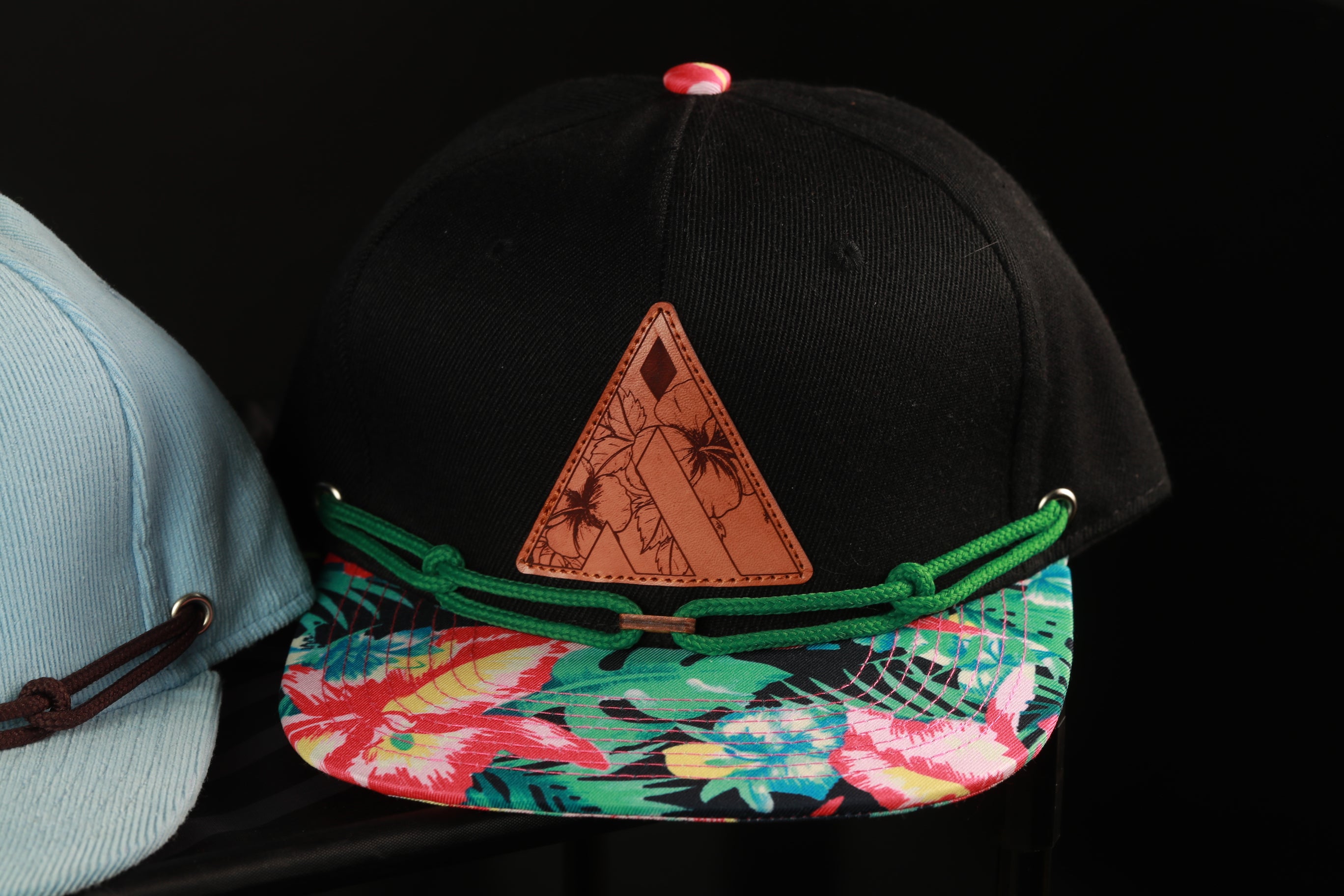 A black baseball cap with a colorful floral pattern and a triangular patch on the front.