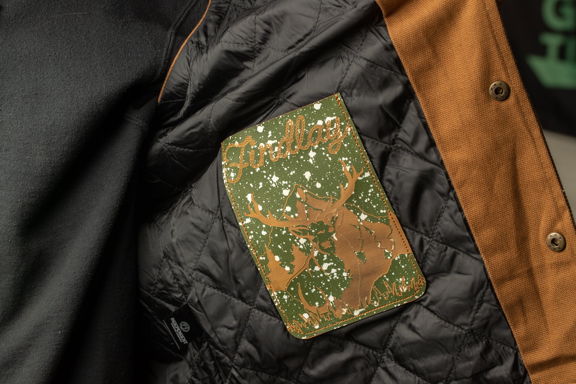 a close-up view of a jacket's lining, featuring a green patch with a deer silhouette and the word "Grail" printed on it.