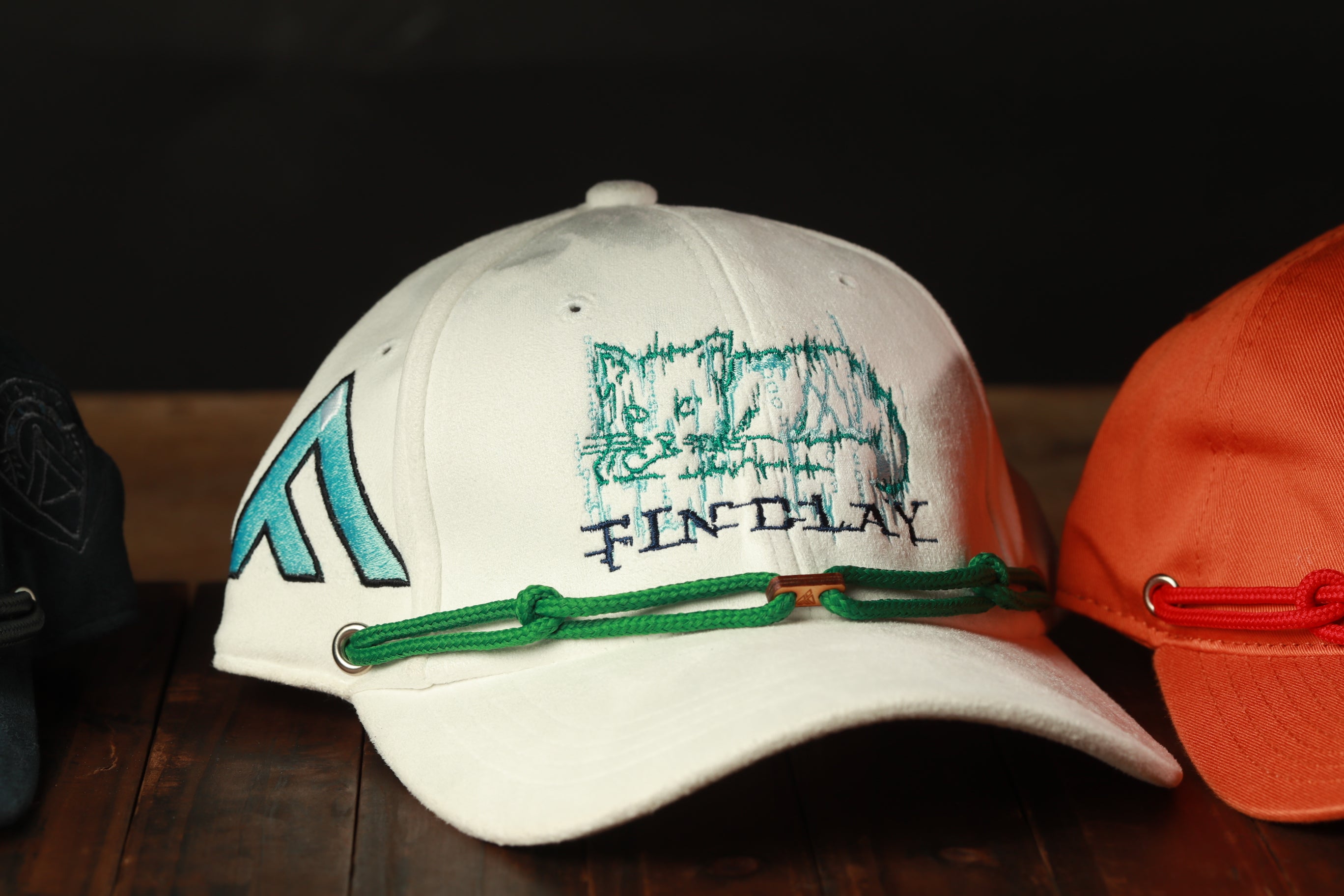 A white baseball cap with a cat design and the text "FIND LAY" printed on it, along with a green string or strap.