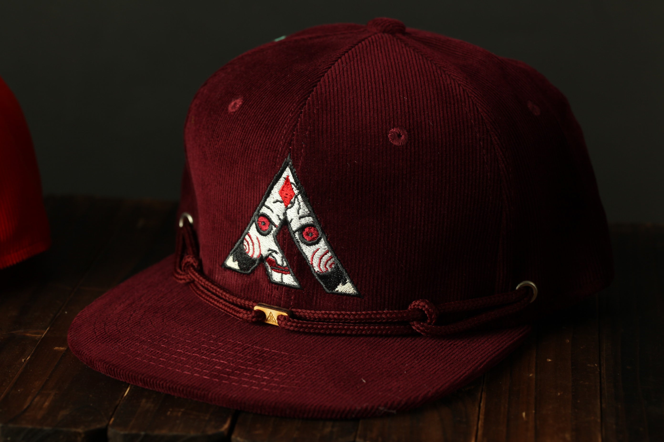 A burgundy baseball cap with a white and black graphic design on the front, sitting on a wooden surface.