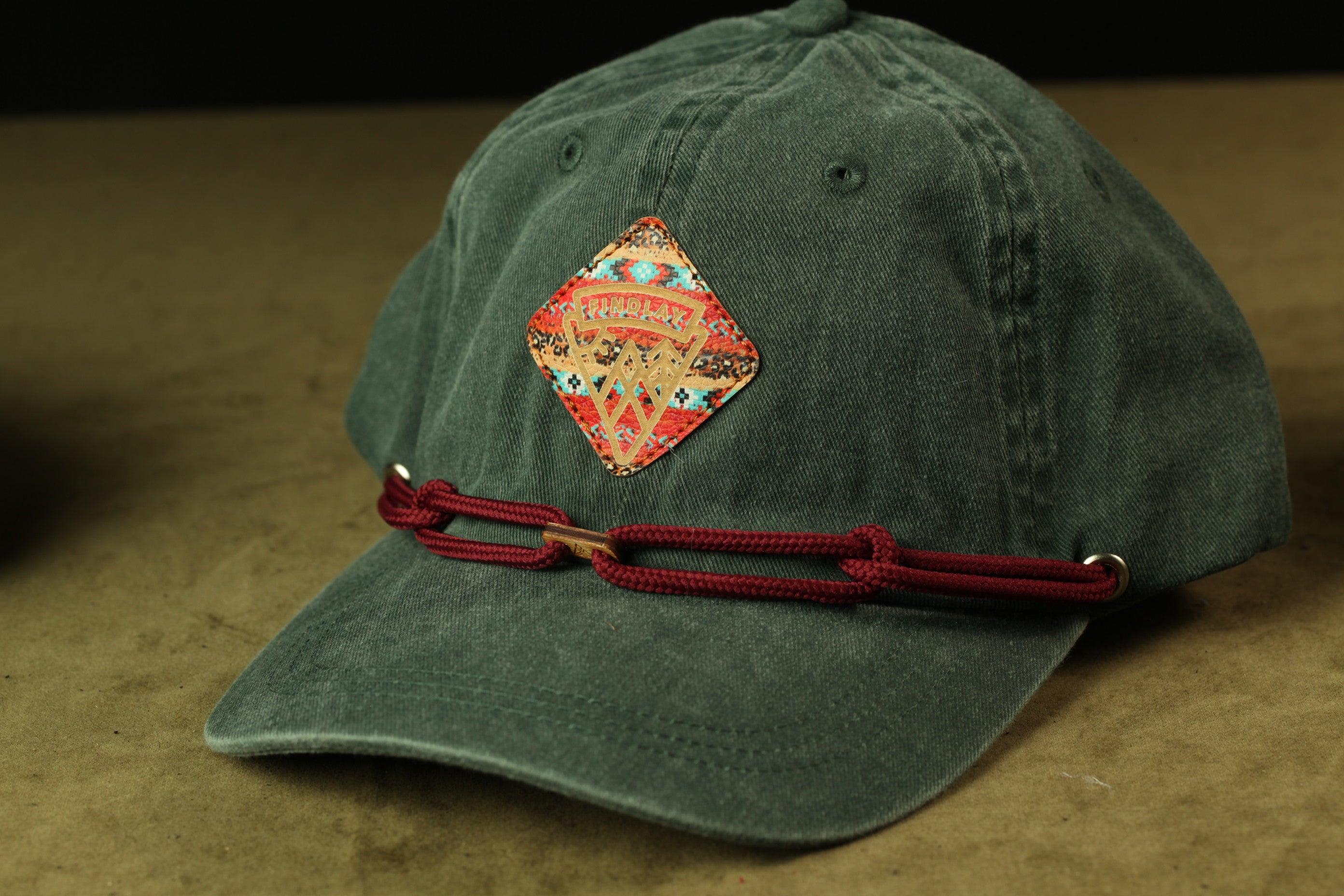 A green baseball cap with a red braided strap and a patch on the front.