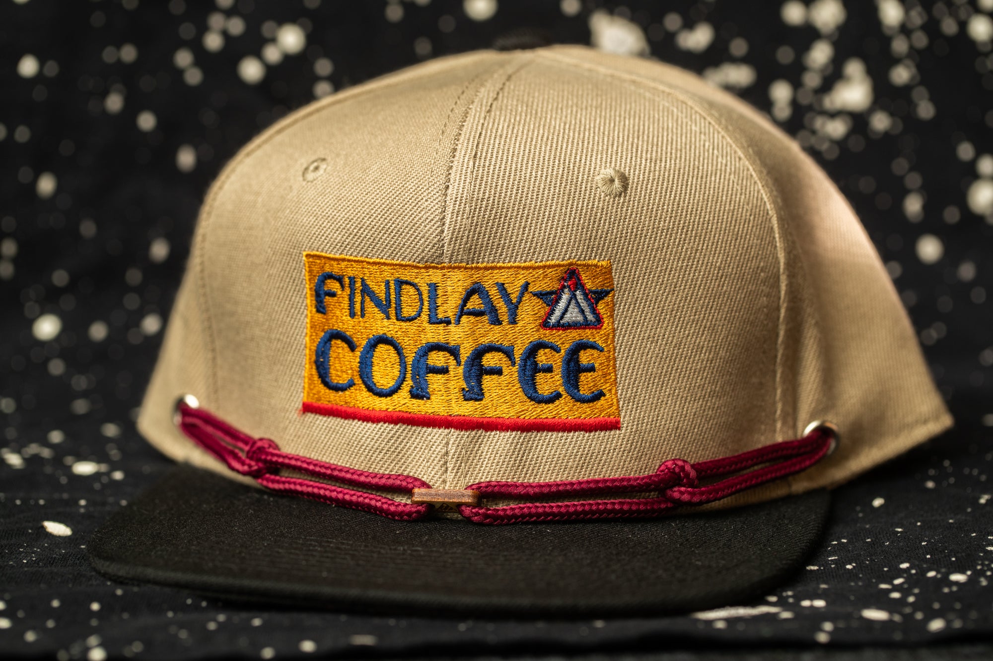 A beige baseball cap with a red string and a patch on the front that says "Findlay Coffee".