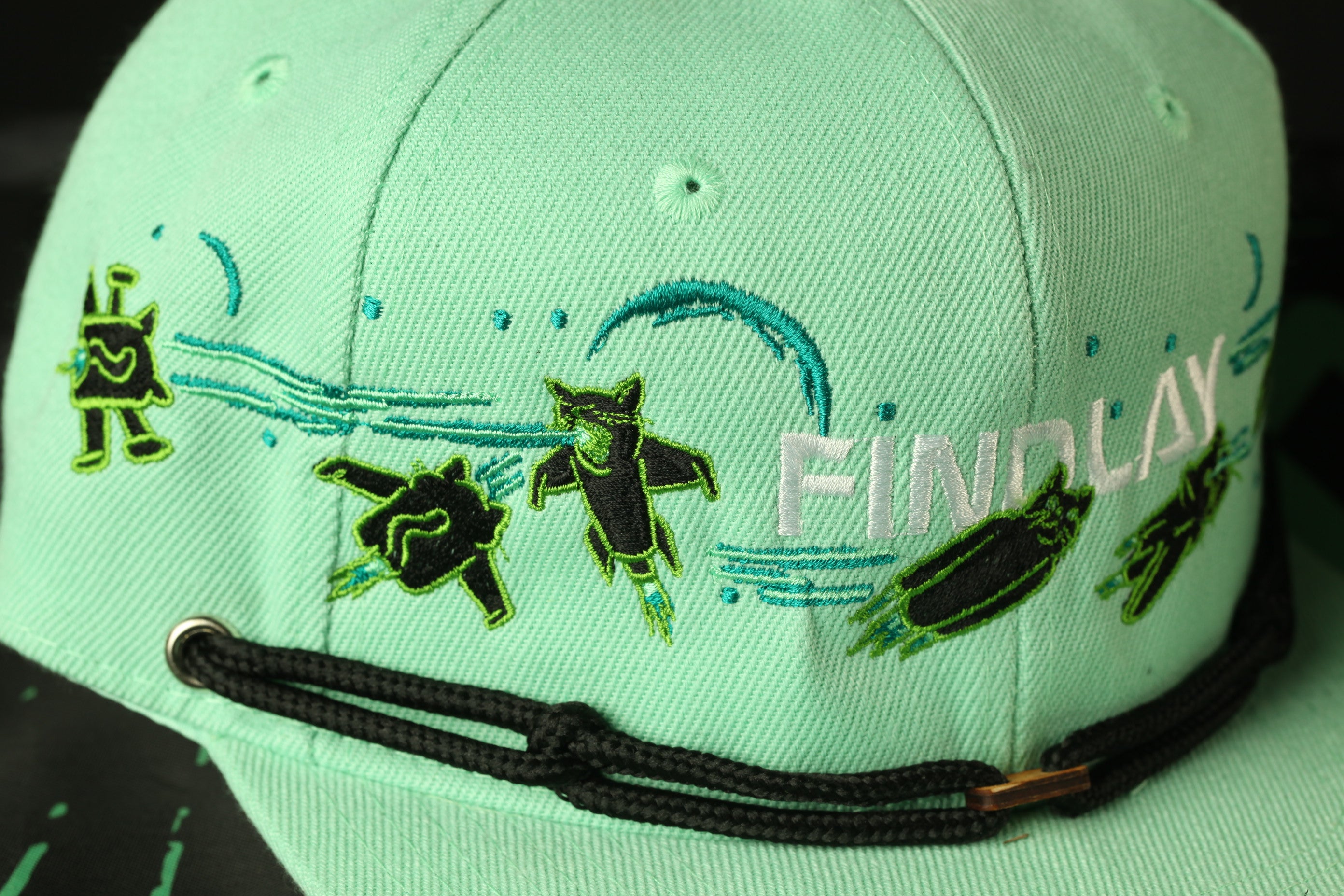 A close-up view of a green baseball cap with various embroidered designs and text.