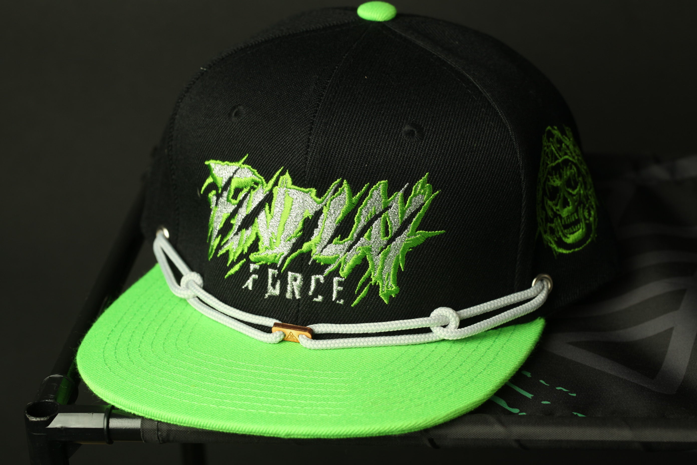 A black baseball cap with green accents, featuring a skull and crossbones design, and the text "TADAX FORCE" printed on it.