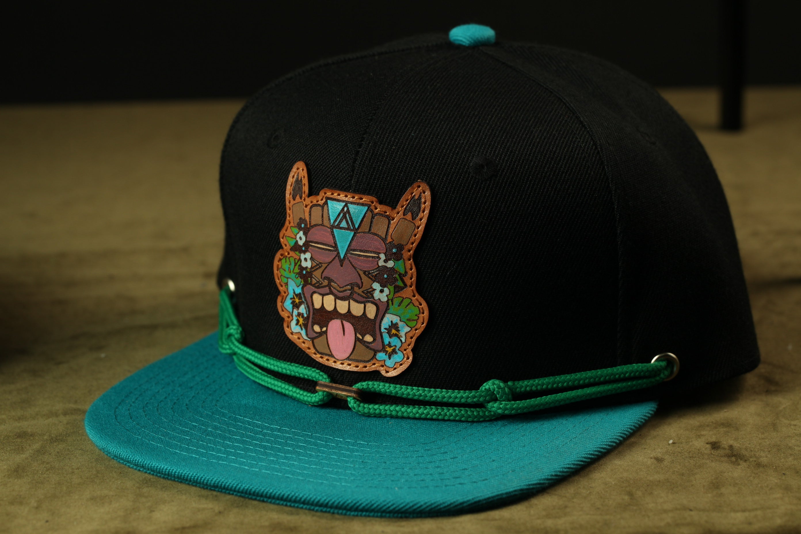 A black baseball cap with a colorful, cartoonish face patch on the front.