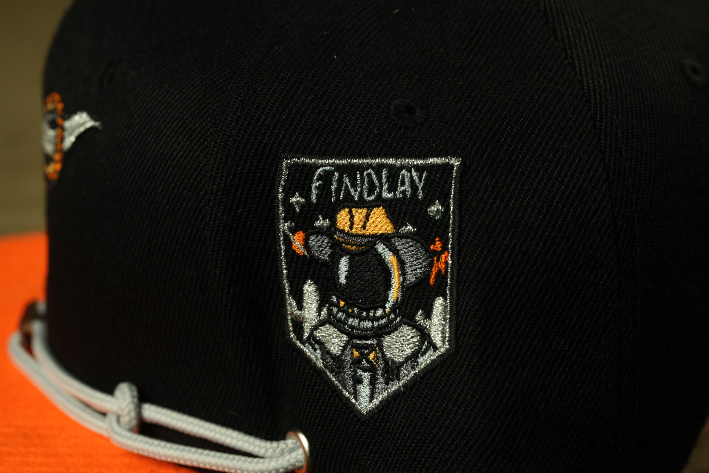 A close-up view of a black baseball cap with a patch featuring an embroidered design and text.