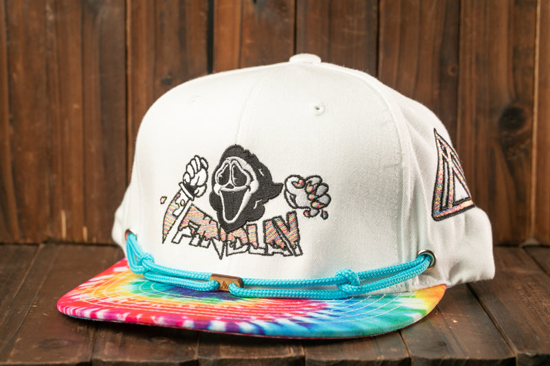A white baseball cap with a tie-dye pattern and a graphic design on the front, placed on a wooden surface.