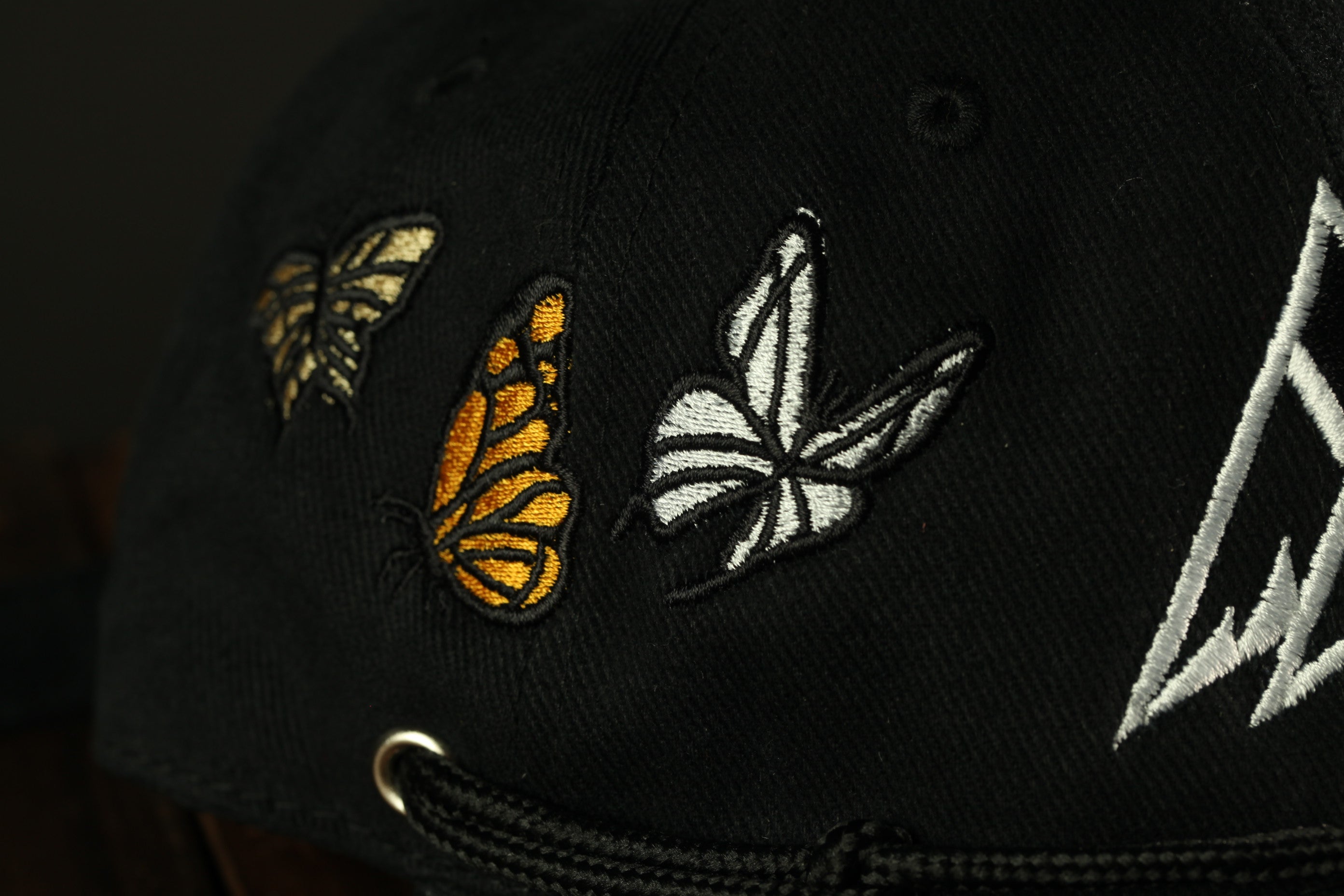 A close-up view of a black baseball cap with three embroidered butterflies on the front.