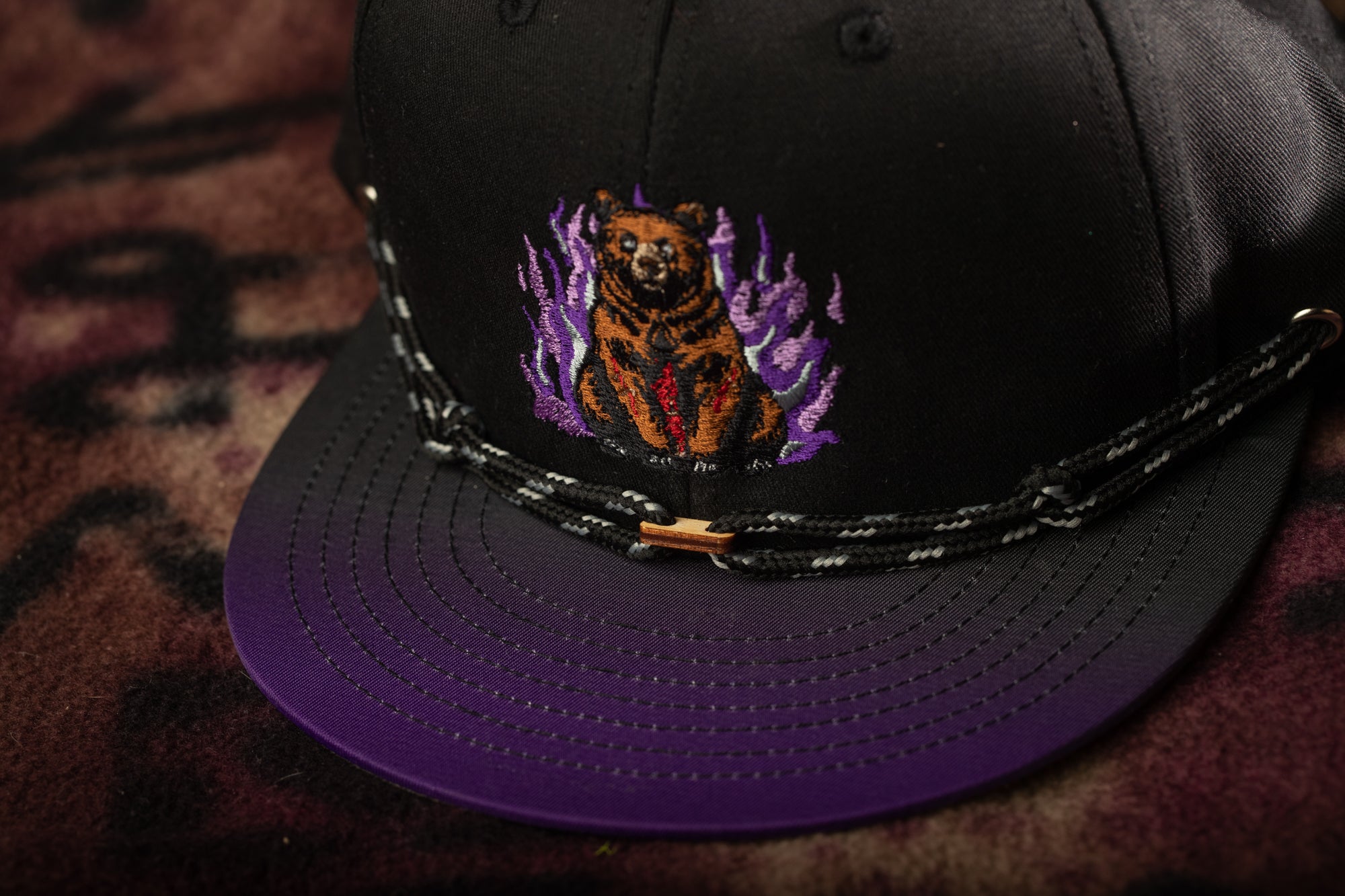 A black baseball cap with a purple brim and a bear embroidered on the front.
