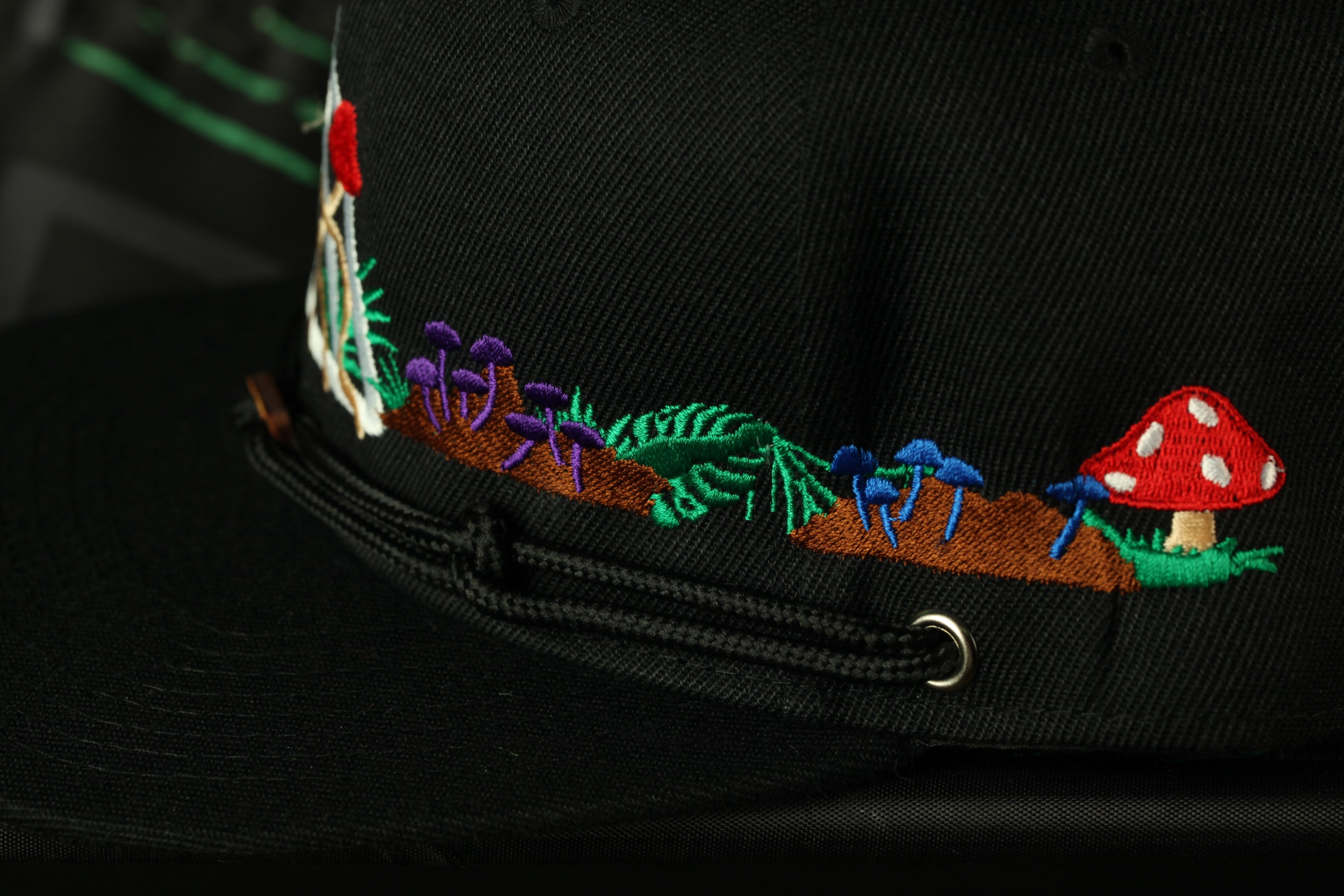 a close-up view of a black hat with colorful embroidered designs, including a mushroom, flowers, and leaves.