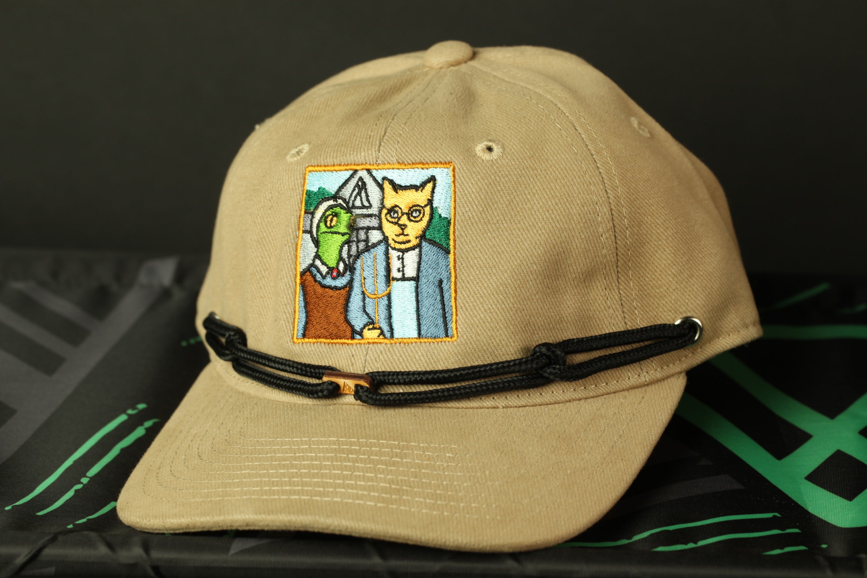 A beige baseball cap with a patch featuring a cartoon cat and a woman.