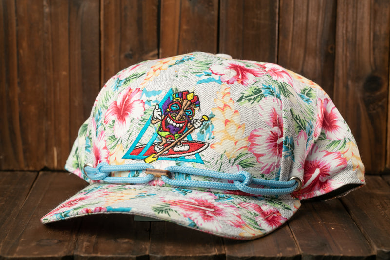 A colorful floral patterned baseball cap with a cartoon character design is displayed on a wooden surface.