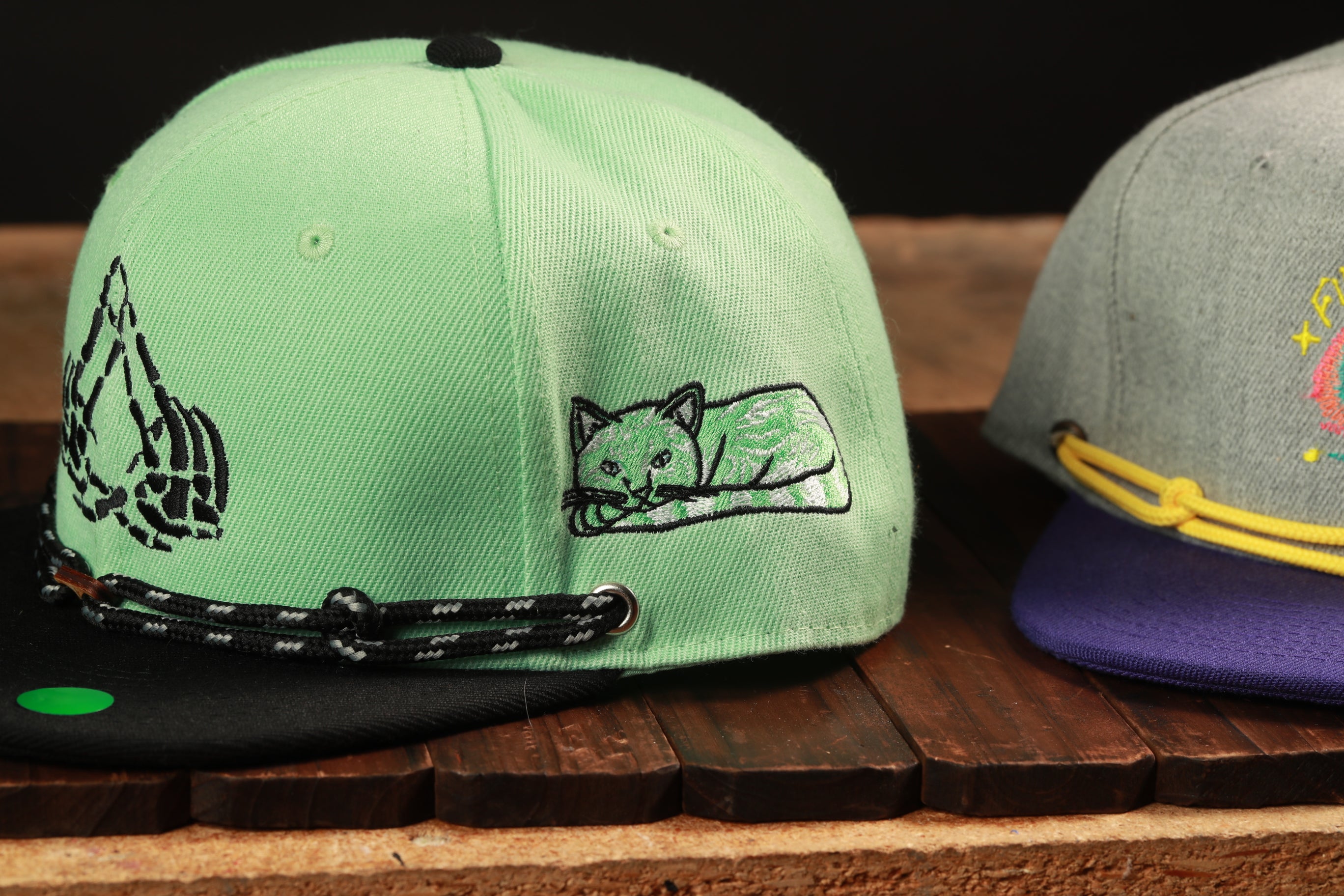 Two baseball caps are displayed on a wooden surface, one green and one gray.