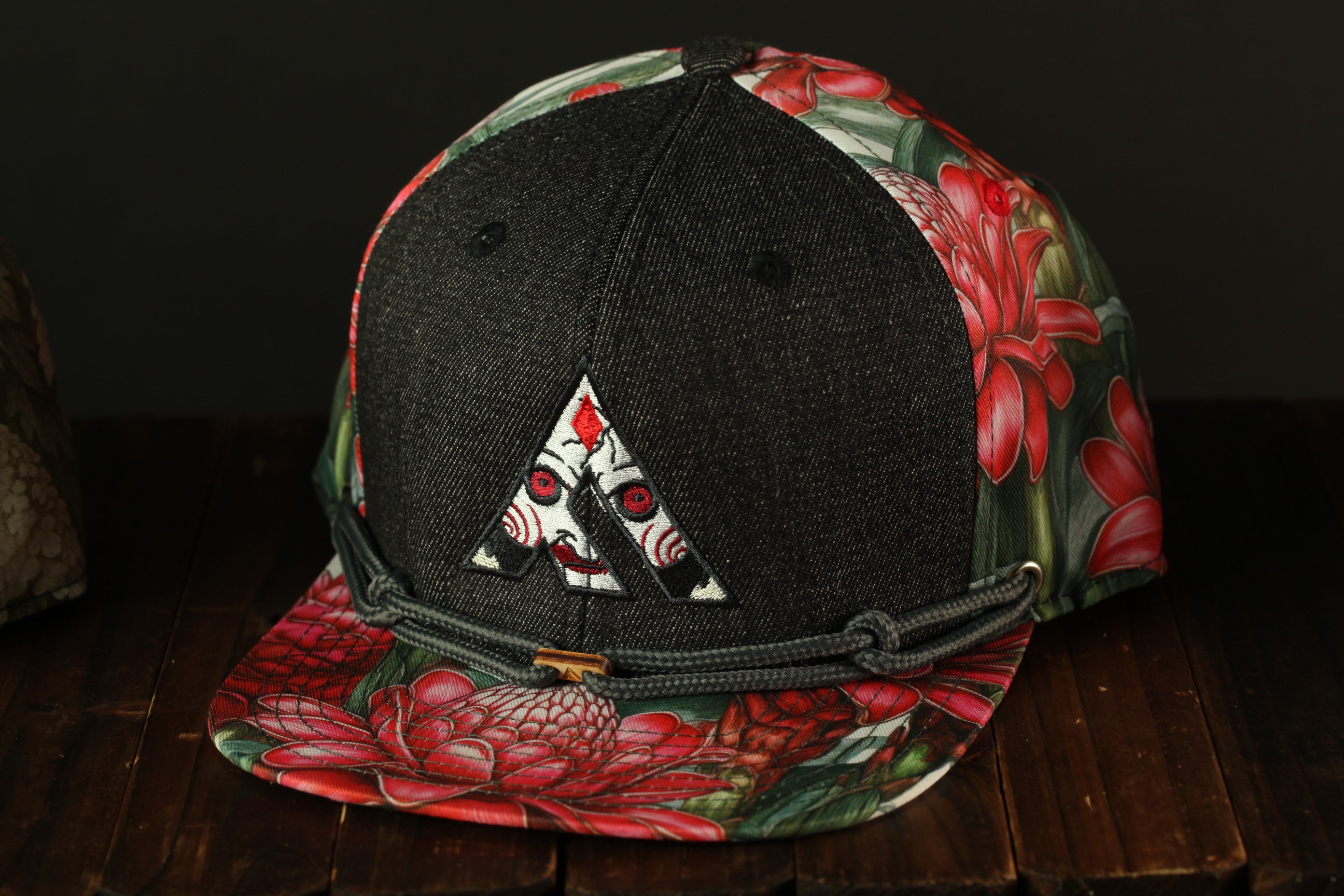 A black baseball cap with a floral pattern and a white triangle logo on the front, placed on a wooden surface.