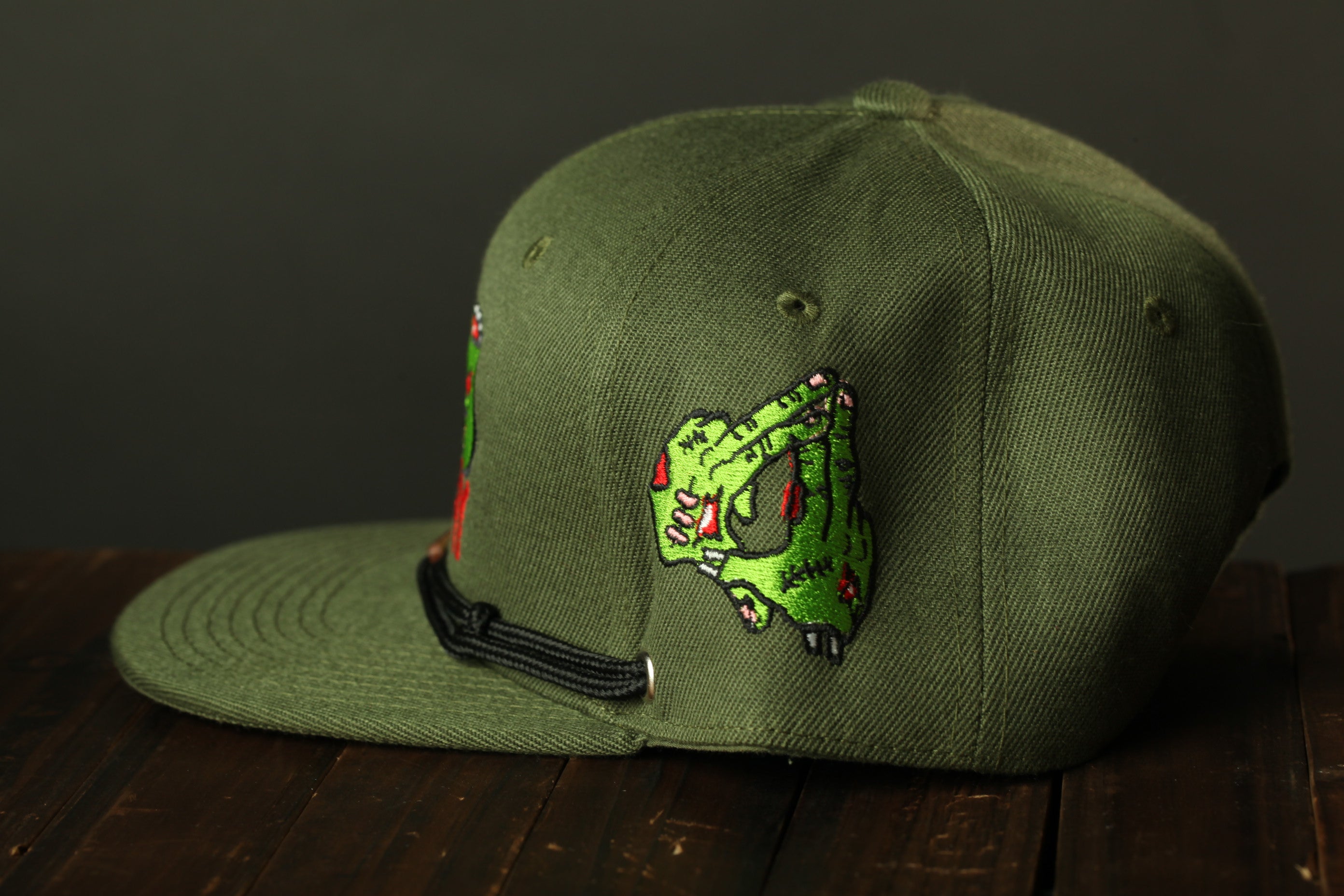 A green baseball cap with a graphic design on the side, sitting on a wooden surface.