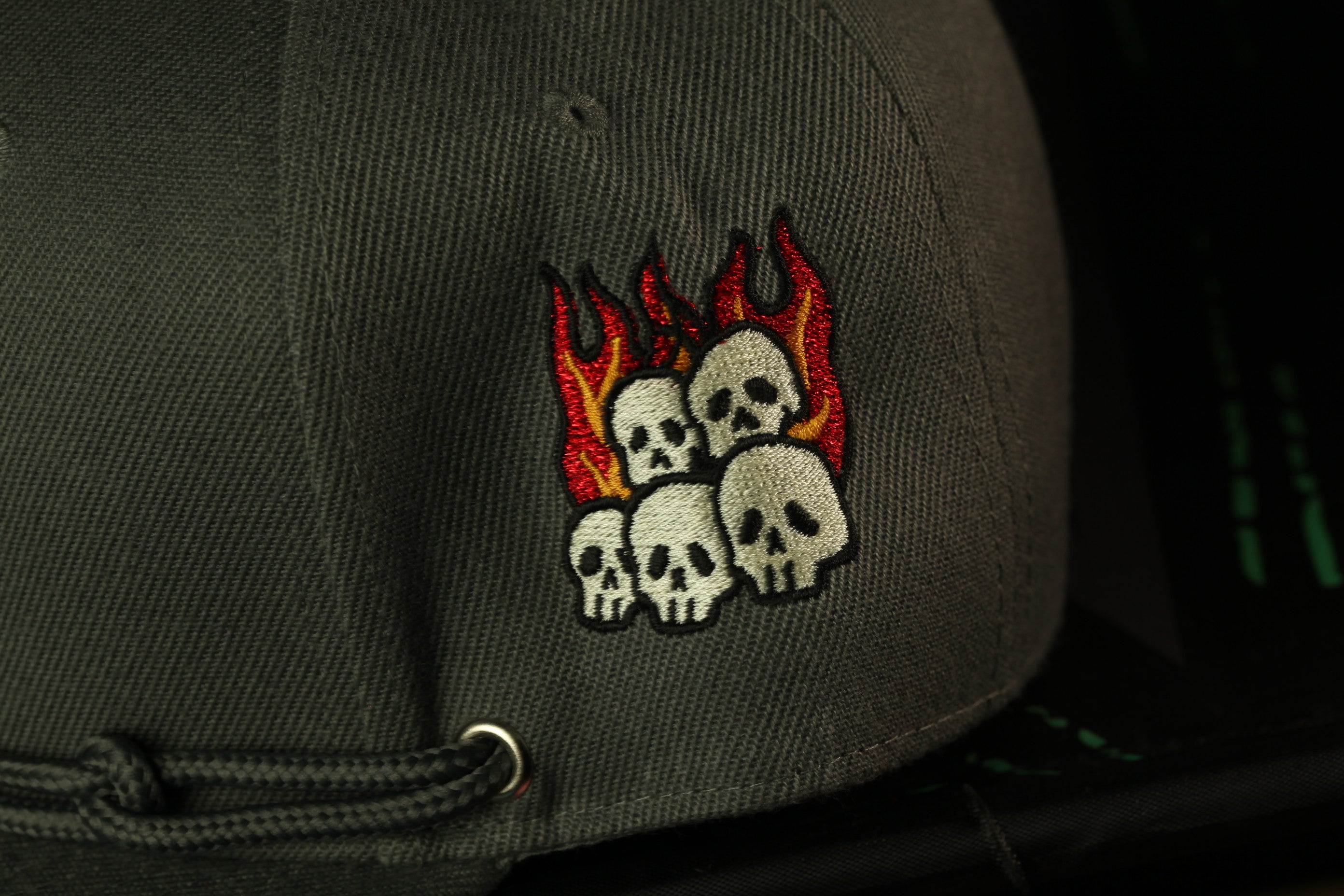 a close-up view of a gray baseball cap with an embroidered design featuring a group of white skulls with flames around them.