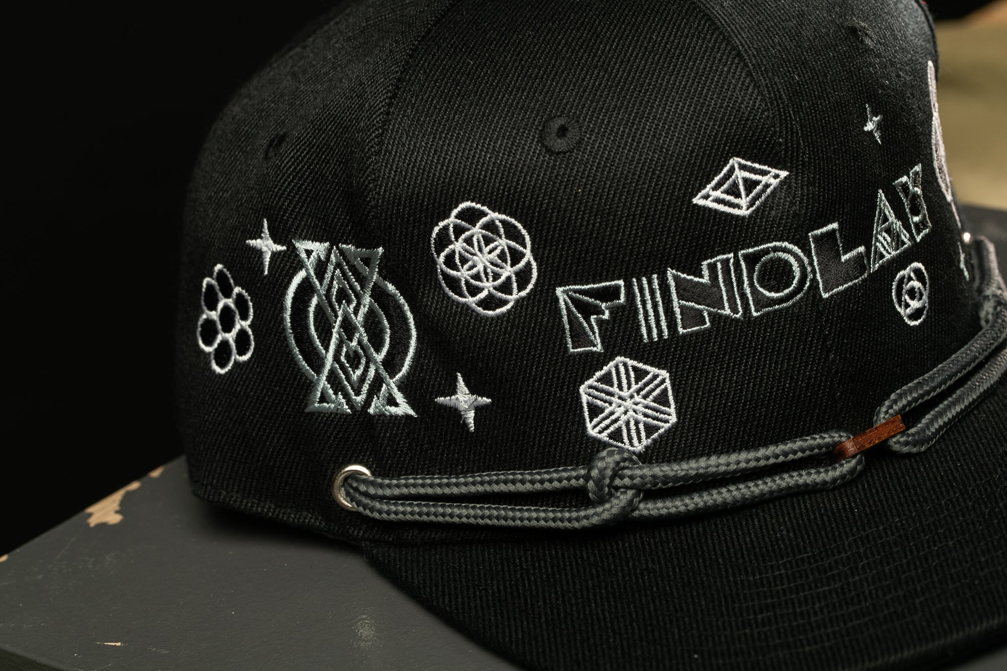 A close-up view of a black baseball cap with various embroidered designs and text on it.