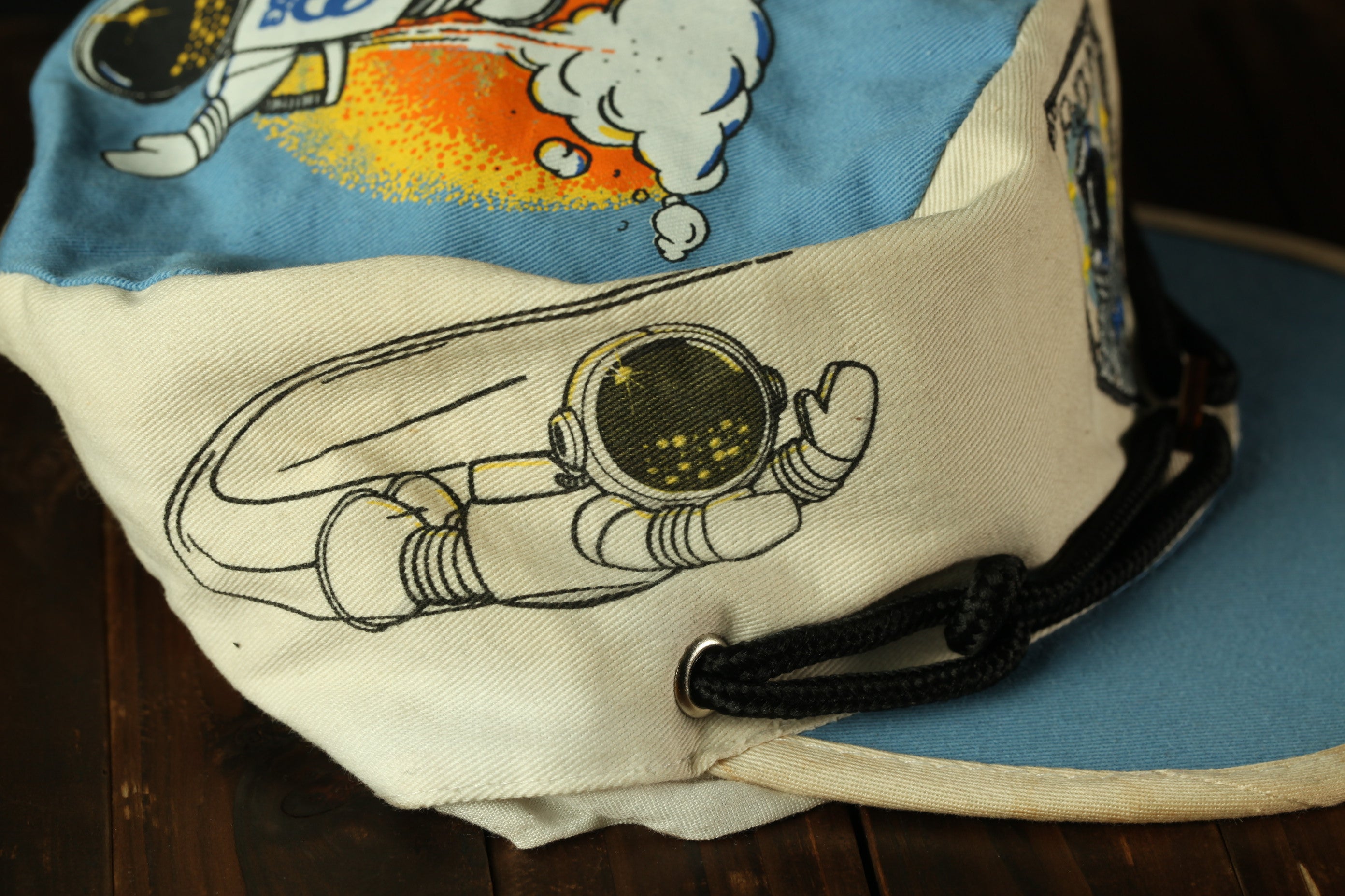 A close-up view of a cap with a space-themed design, including a space helmet and a rocket ship.