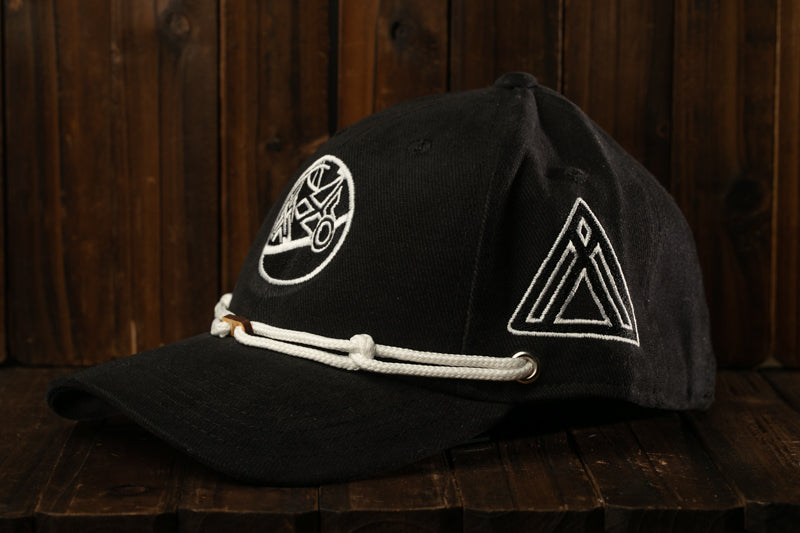 A black baseball cap with white embroidered designs on the front and back, resting on a wooden surface.