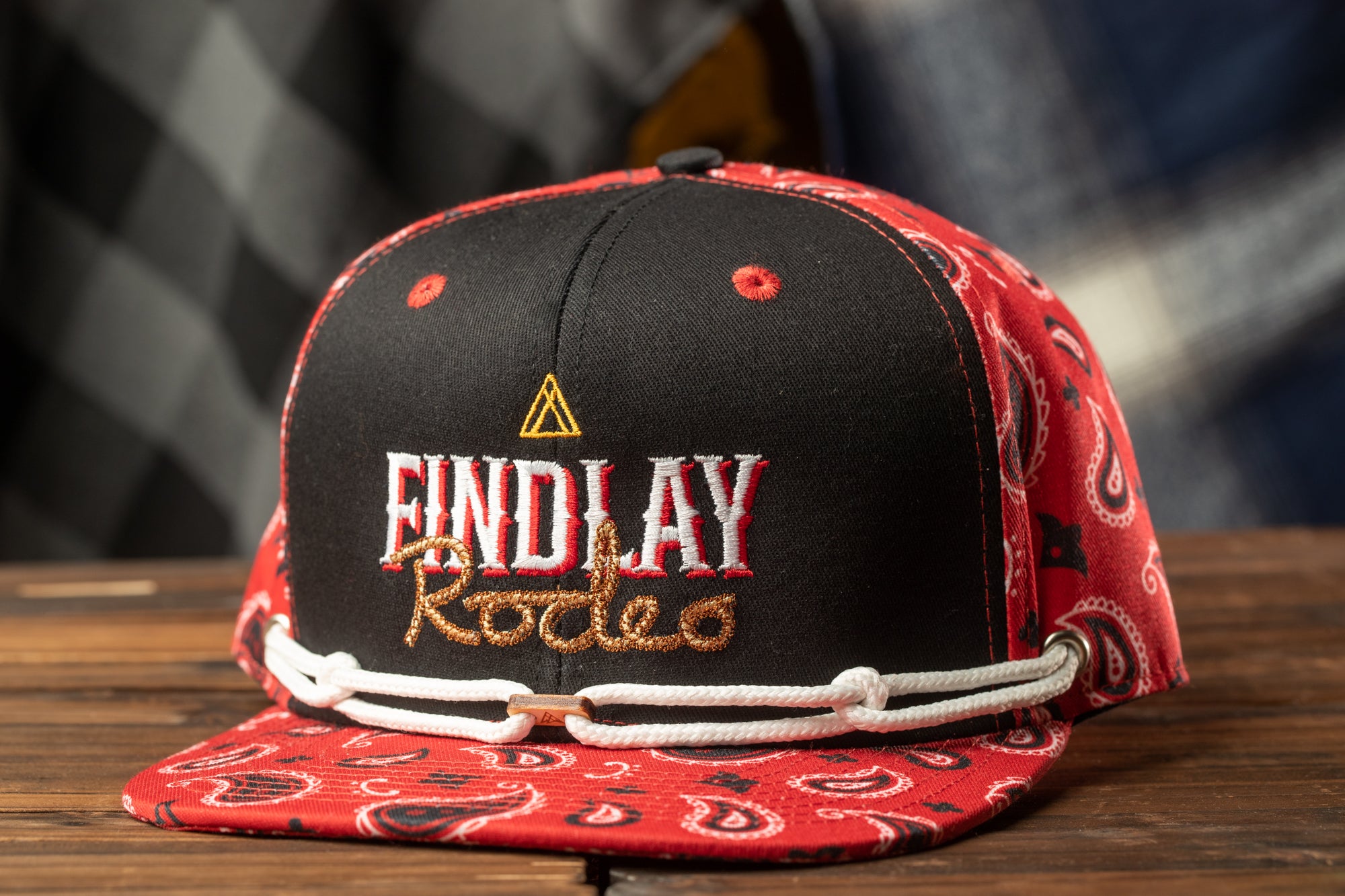 A red and black baseball cap with the text "FIND LAY Rodeo" printed on it, sitting on a wooden surface.