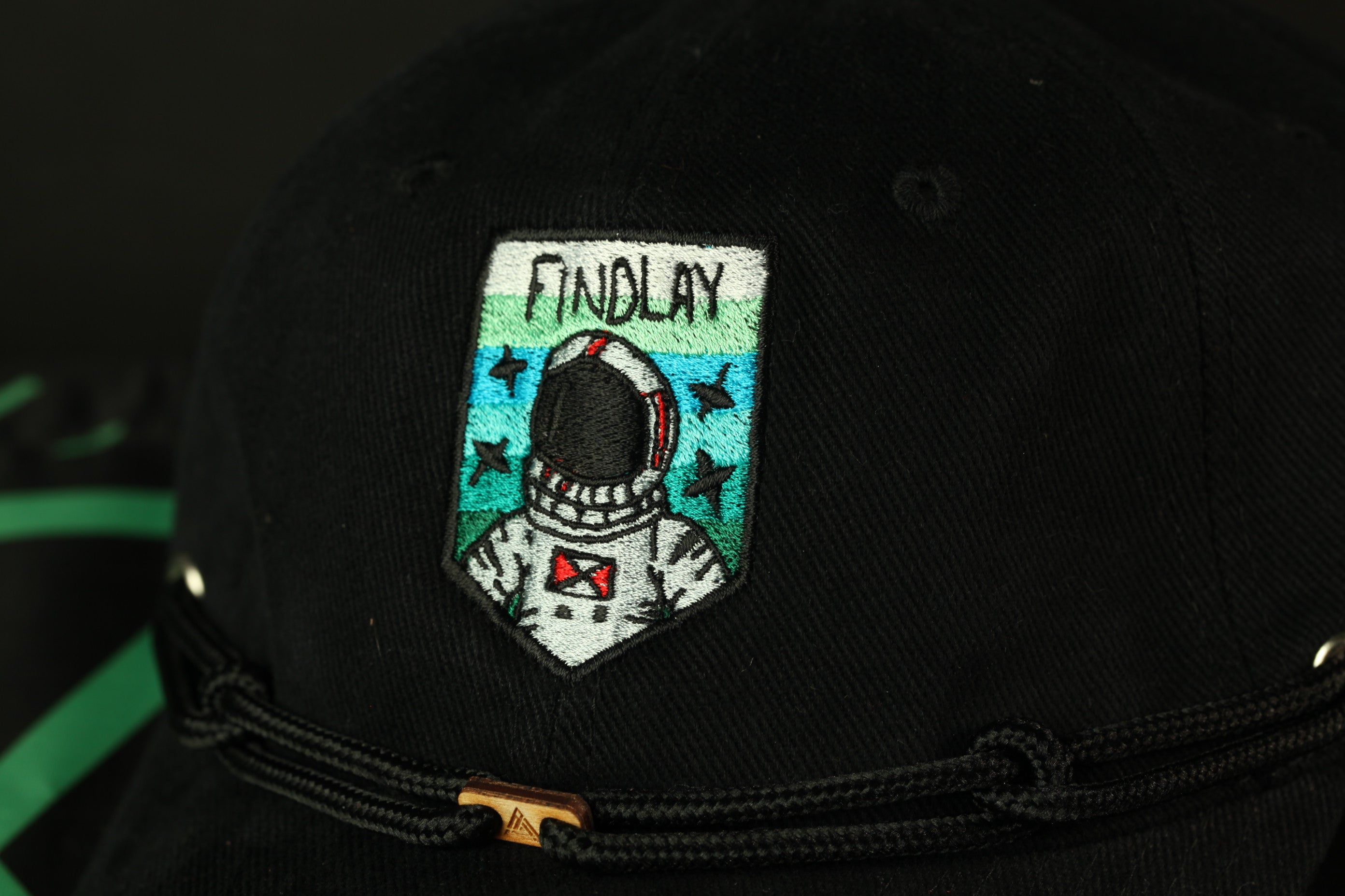 A close-up view of a black baseball cap with a patch featuring an astronaut and the word "FINDLAY" printed on it.