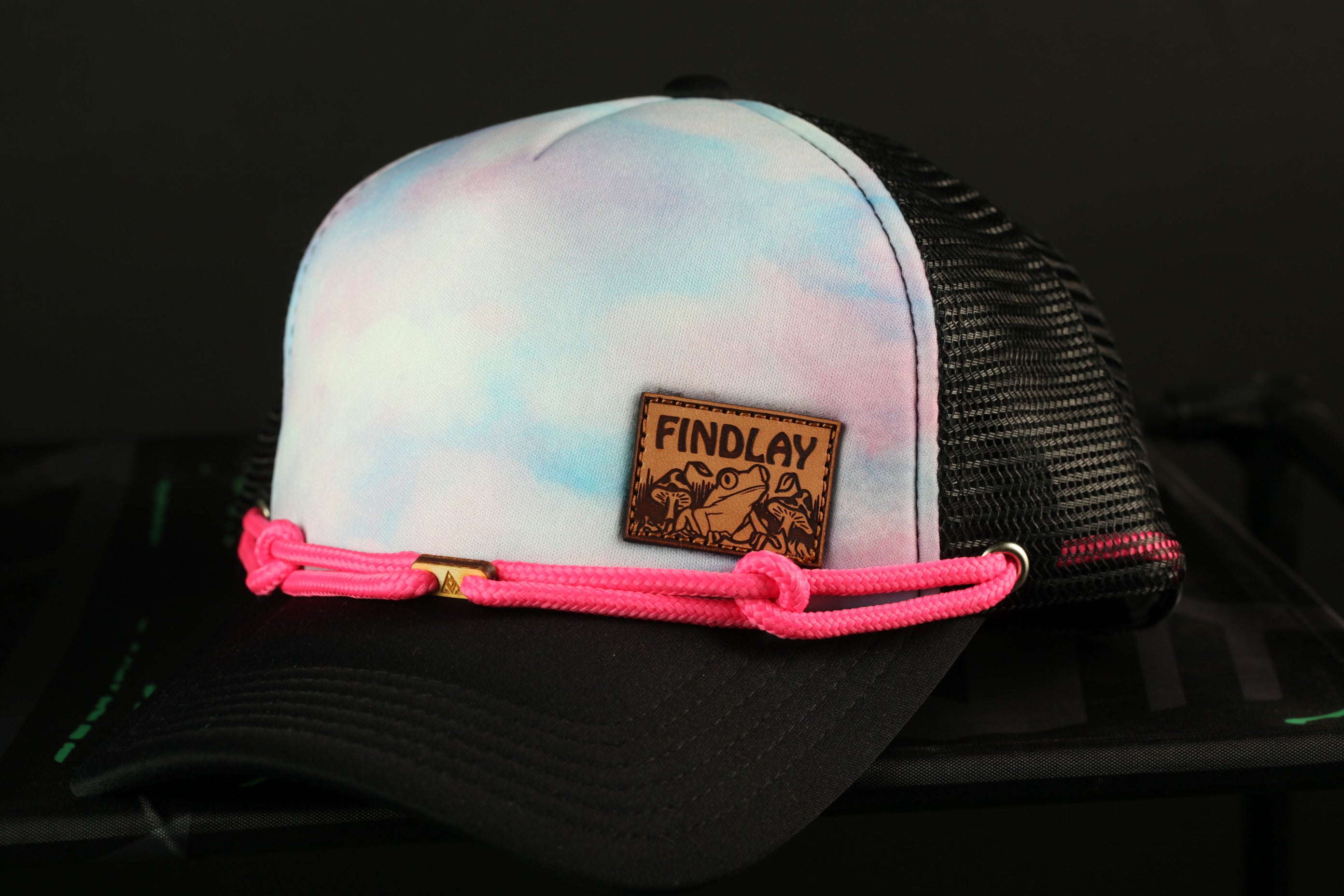 A colorful trucker hat with a black mesh panel and a pink braided strap.