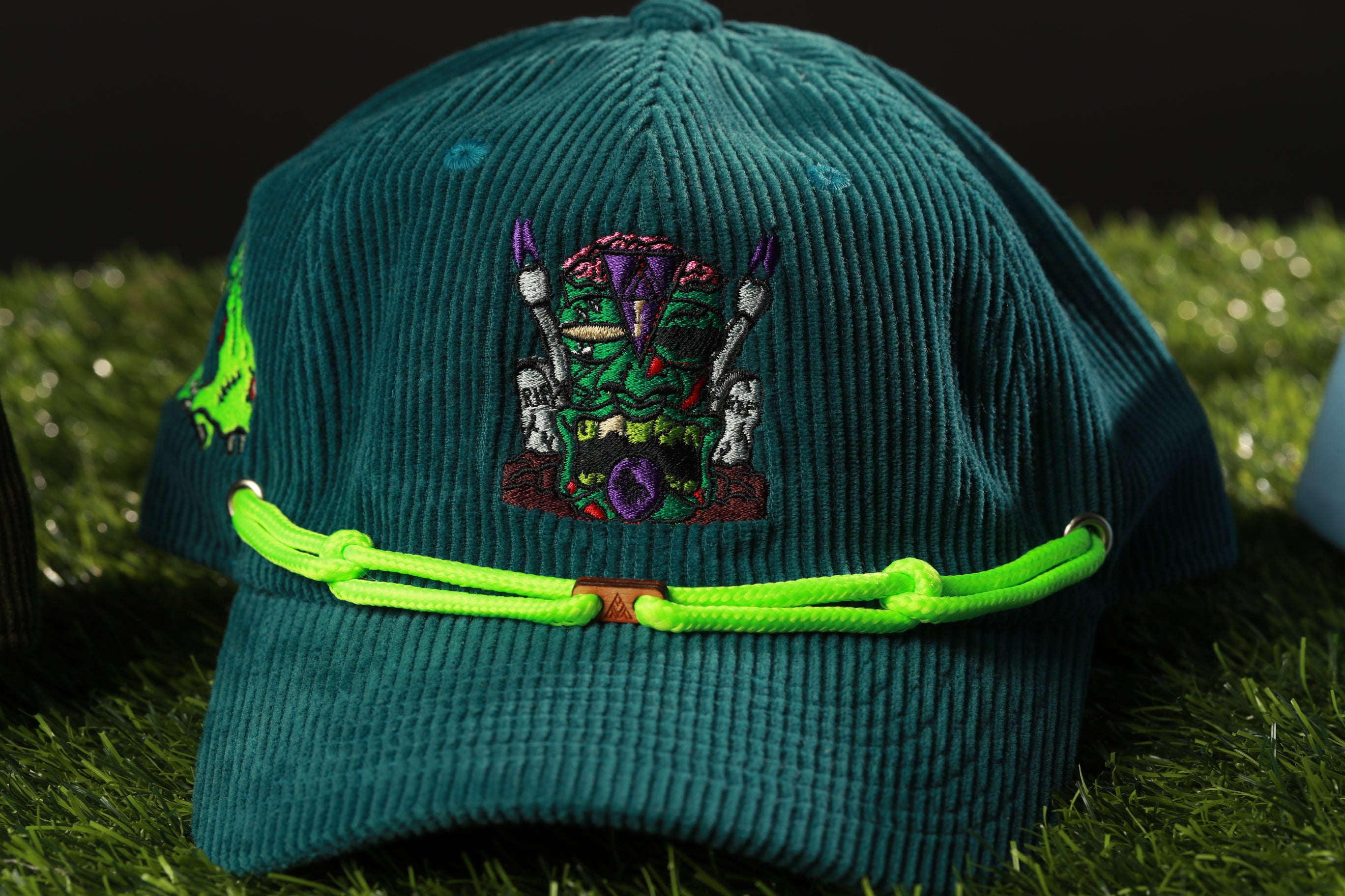 A green baseball cap with a colorful, cartoonish design on the front, featuring a monster or creature with a purple face and green body.
