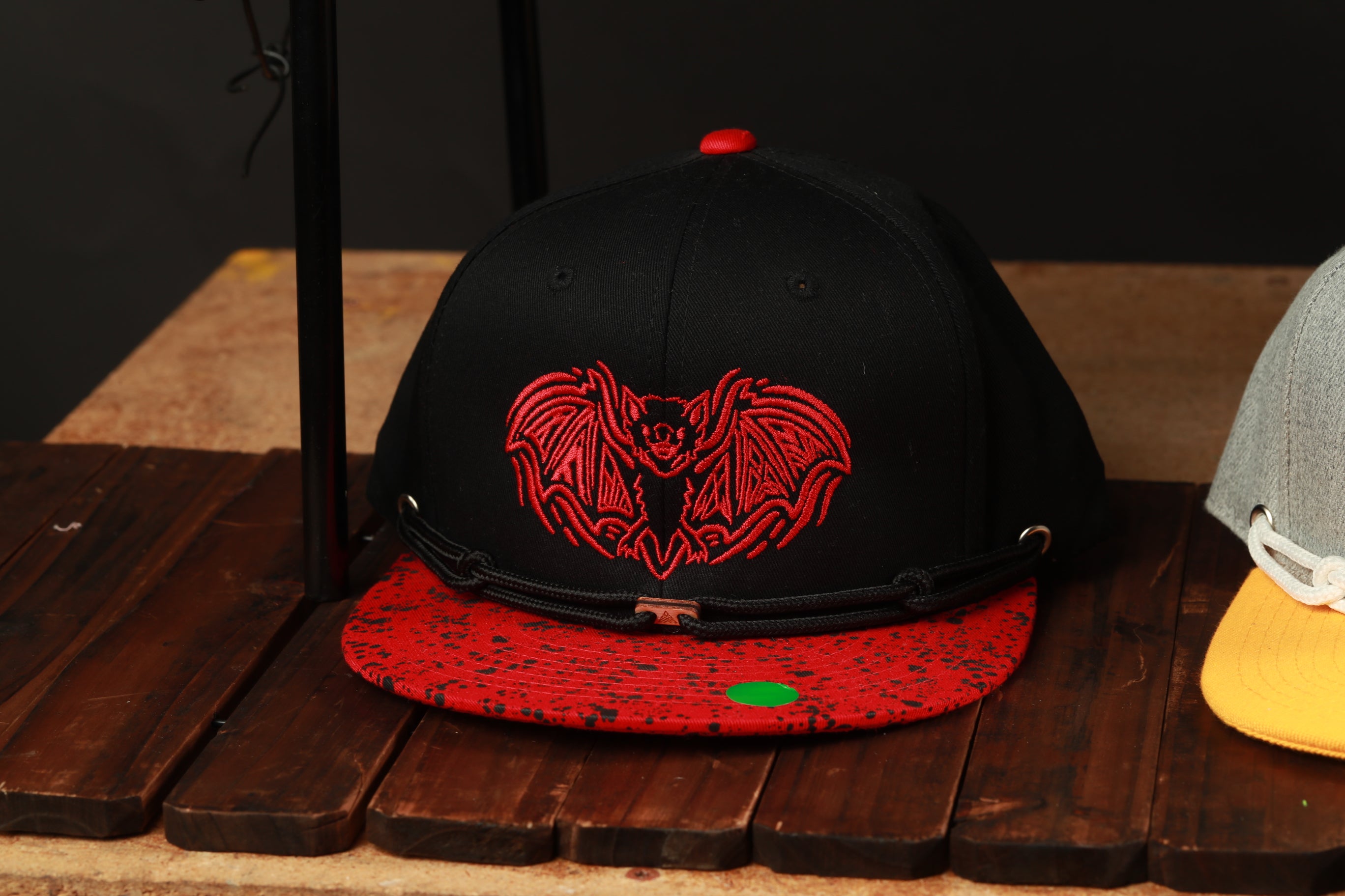 A black baseball cap with a red bat design is displayed on a wooden surface.