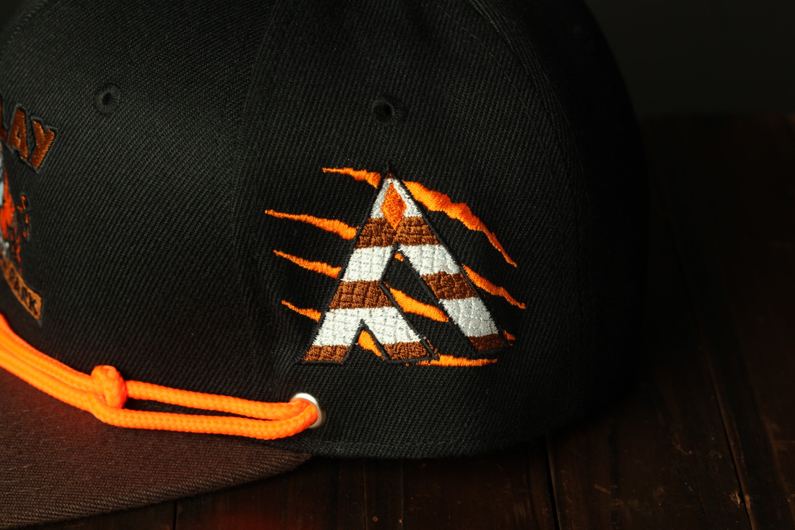 A close-up view of a black baseball cap with an orange and white embroidered logo on the front.