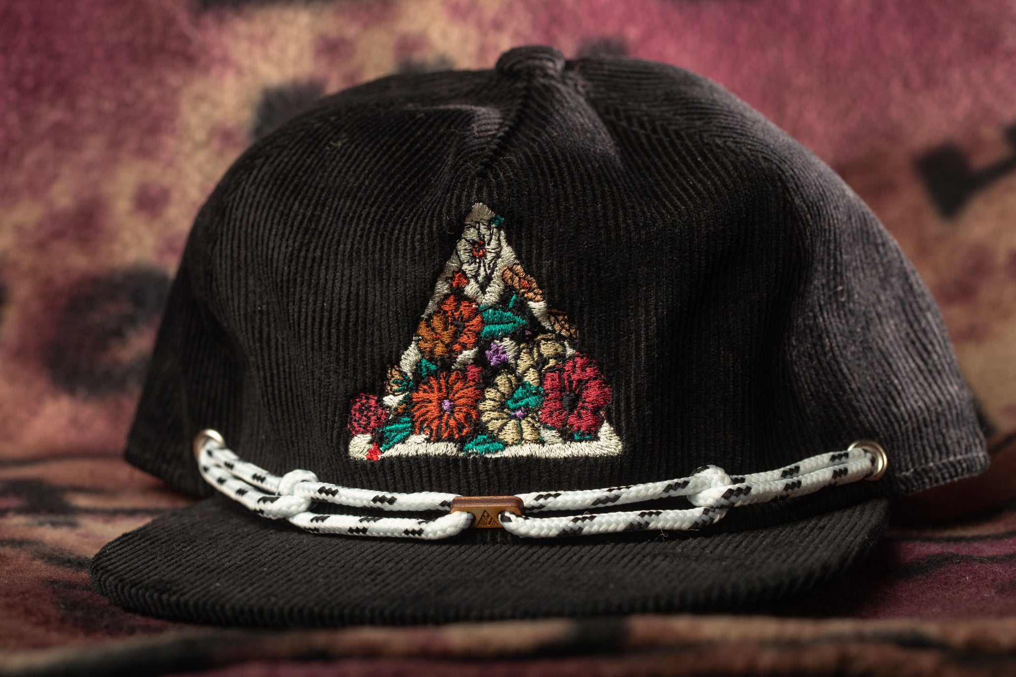 A black baseball cap with a colorful floral embroidered triangle on the front.