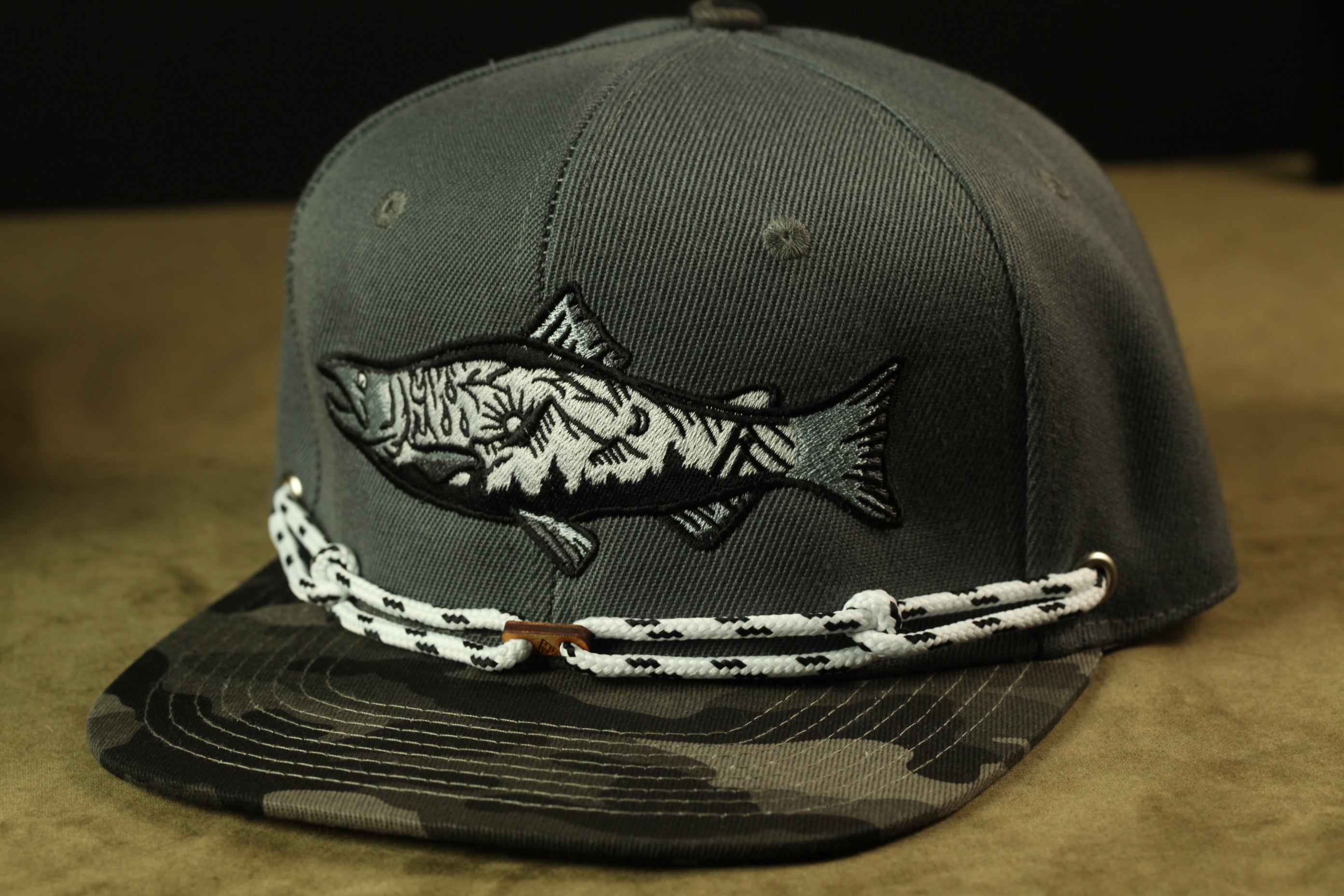 A gray baseball cap with a fish embroidered on it, featuring a camouflage pattern.