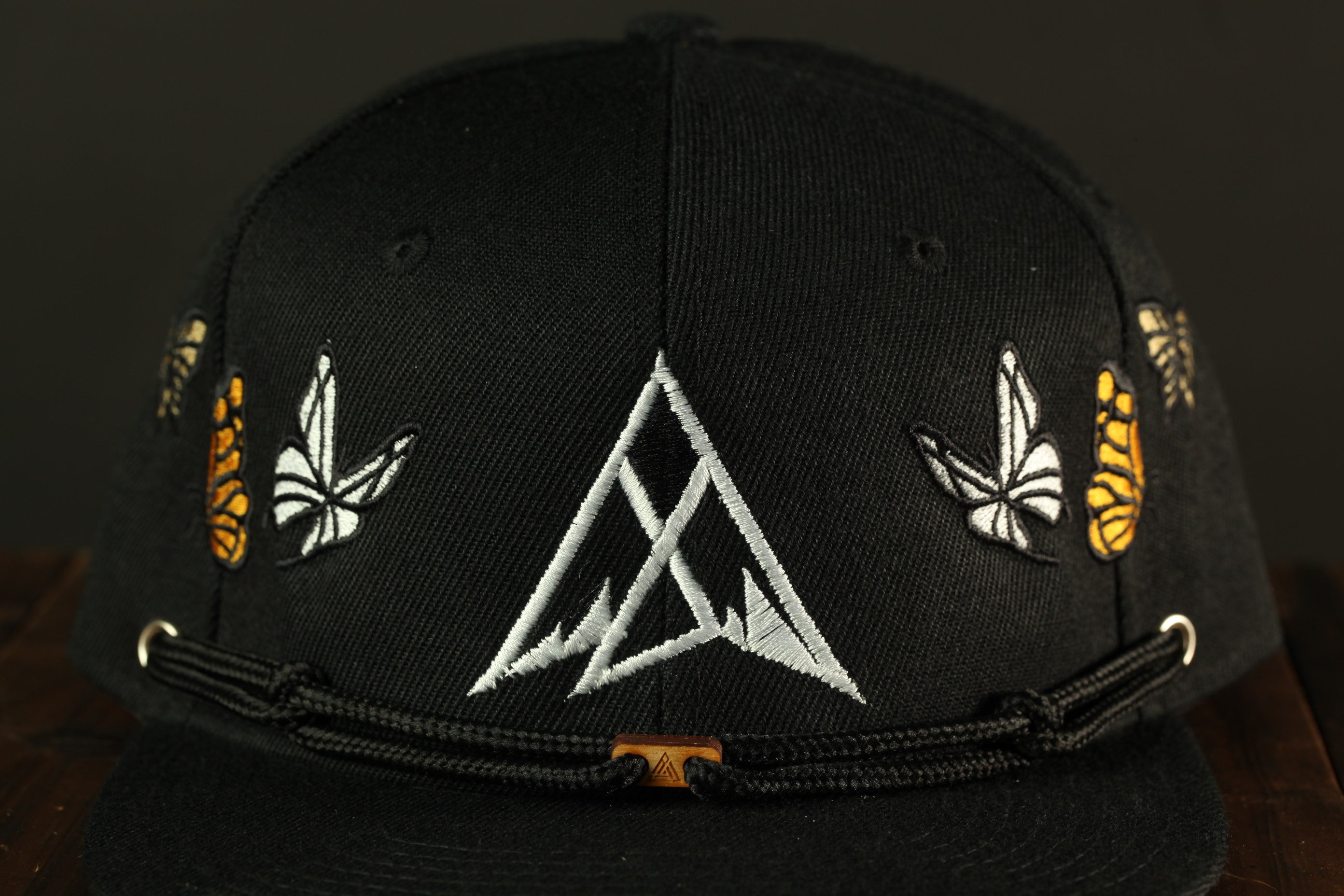 A close-up view of a black baseball cap with a white triangle design and butterflies on the sides.